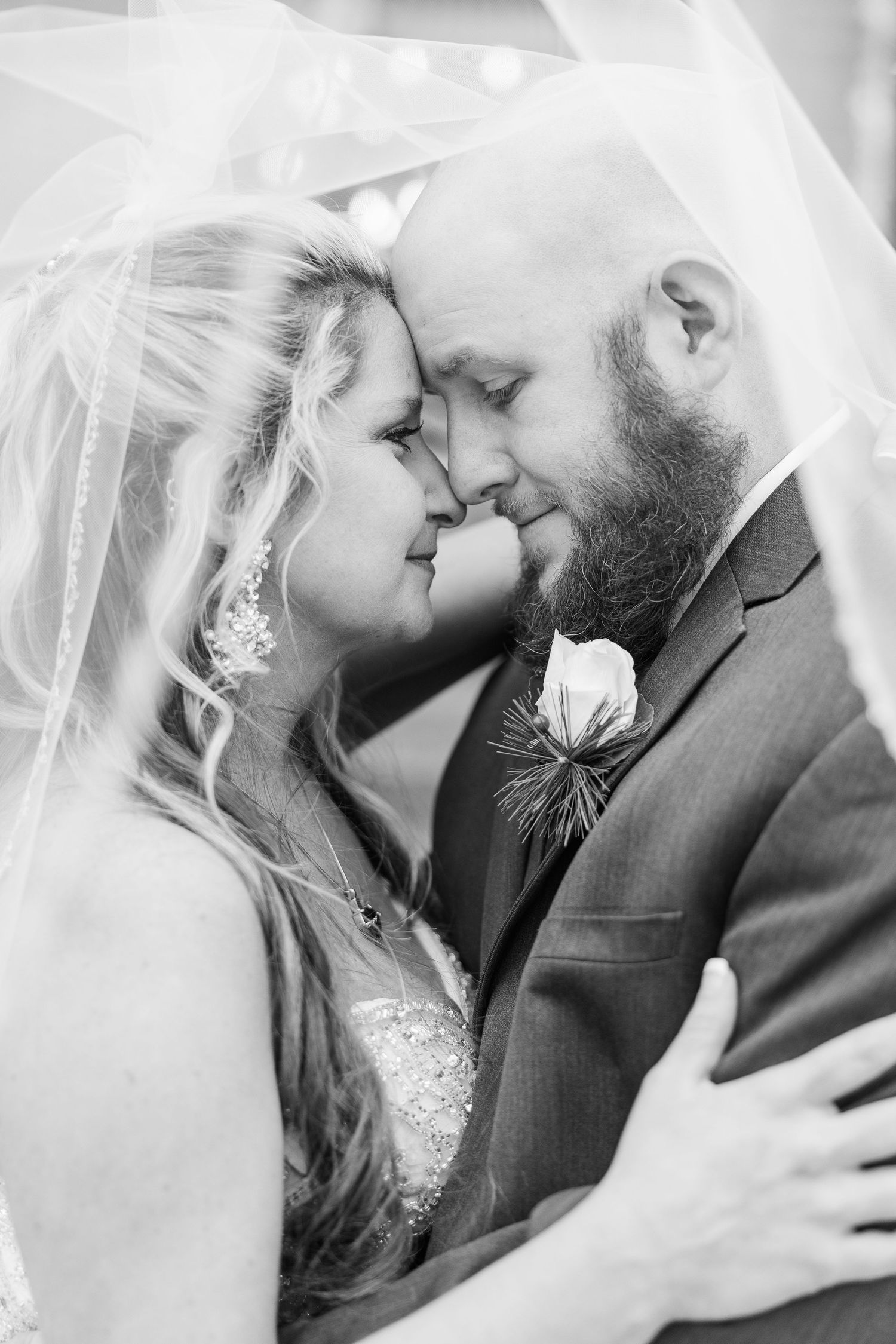 Black and white close-up of tender wedding moment under flowing veil.