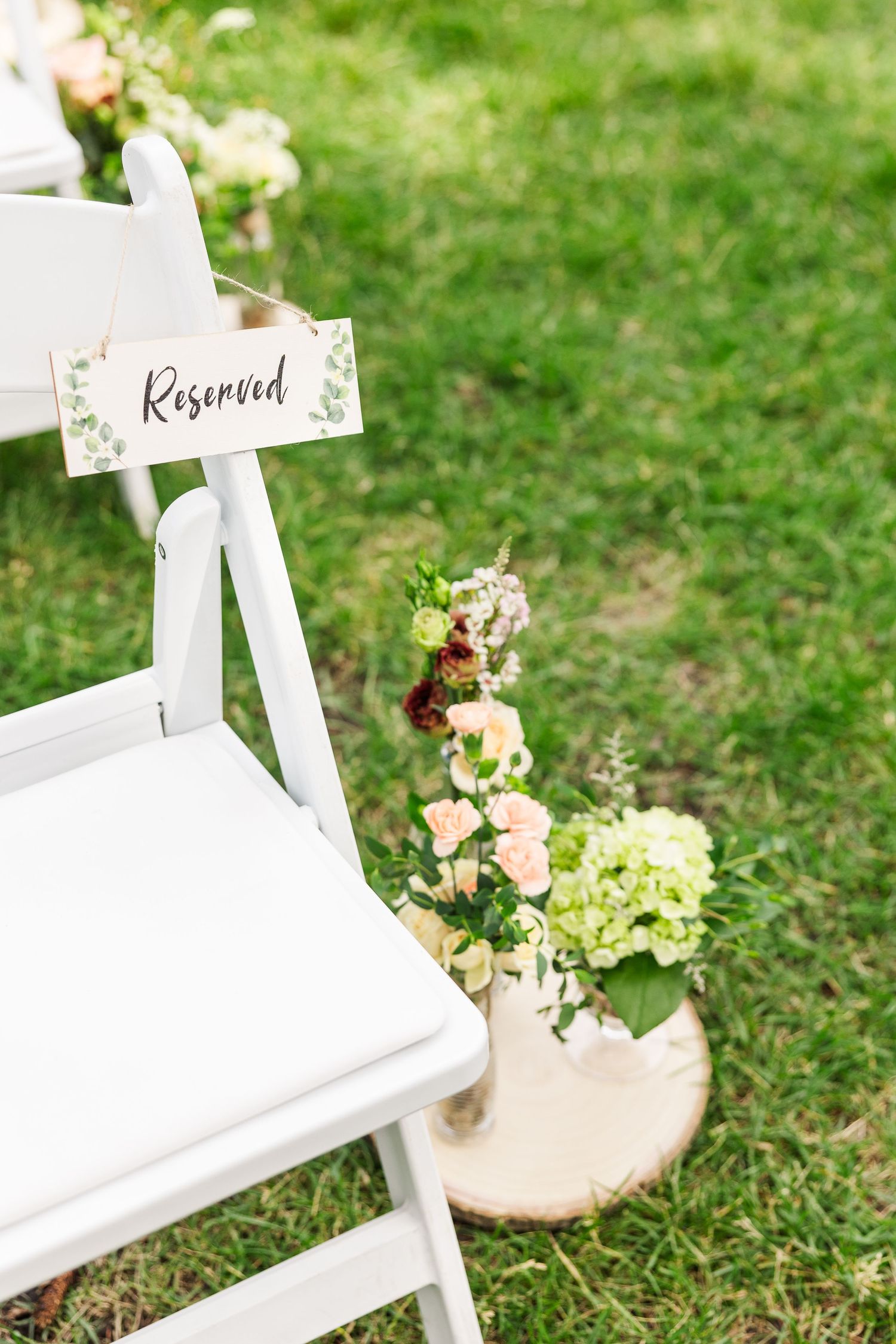 White folding chair with reserved sign and floral decorations at an outdoor wedding setup.