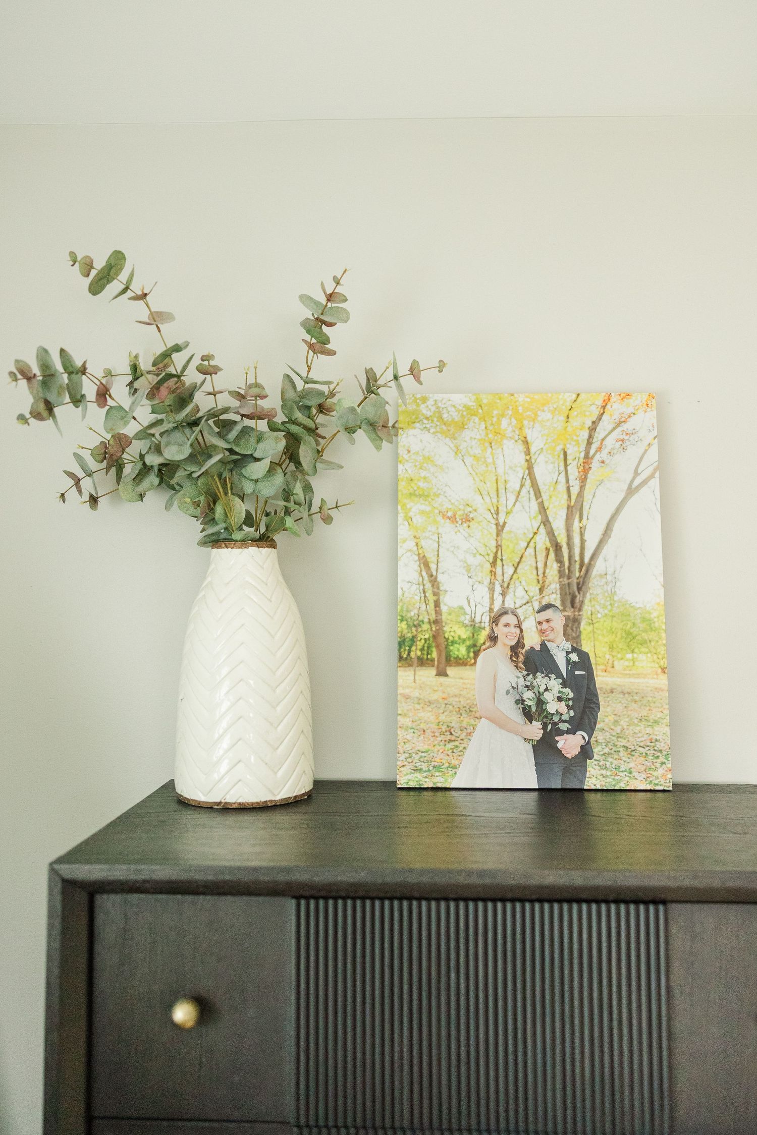 Framed wedding portrait of parents displayed on a dresser with greenery during an in-home lifestyle newborn session in Palatine Illinois