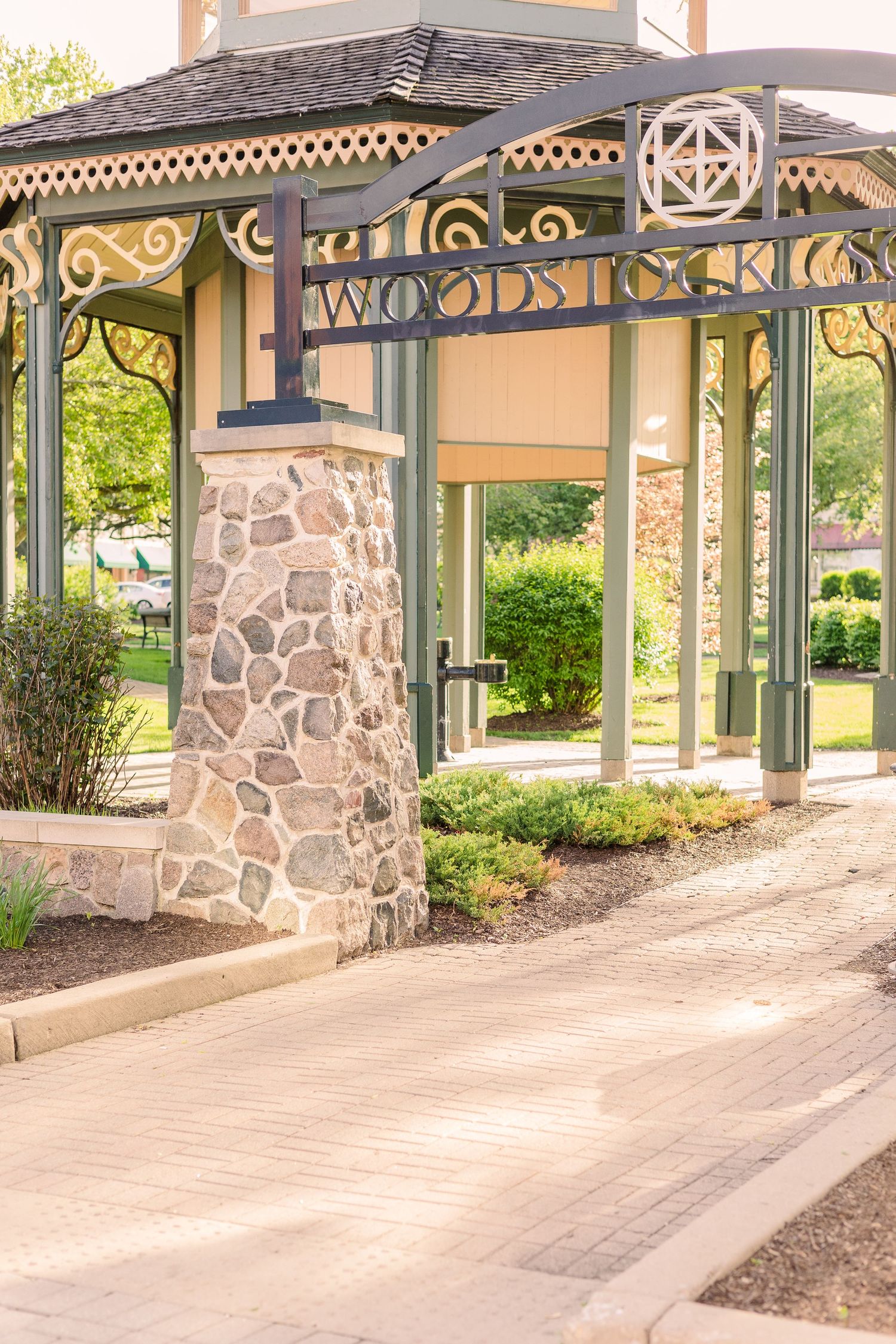 Ornate gazebo entrance with 'Woodstock' sign and stone pillars in park setting.