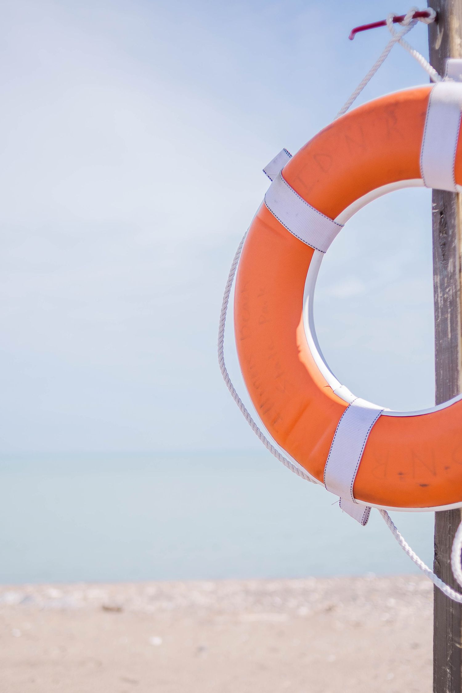 Close-up of orange and white life preserver ring mounted on wooden post against blue sky.