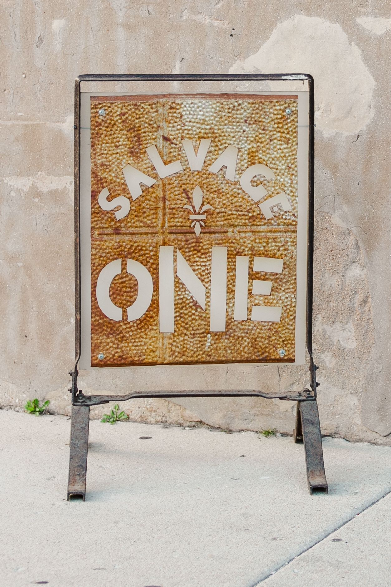 A weathered sign reading 'SALVAGE ONE' mounted on a concrete wall.