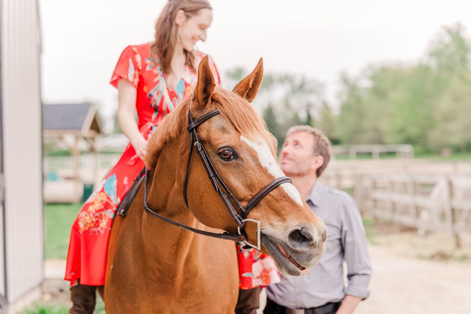 Couple posing with their chestnut horse outside a barn.