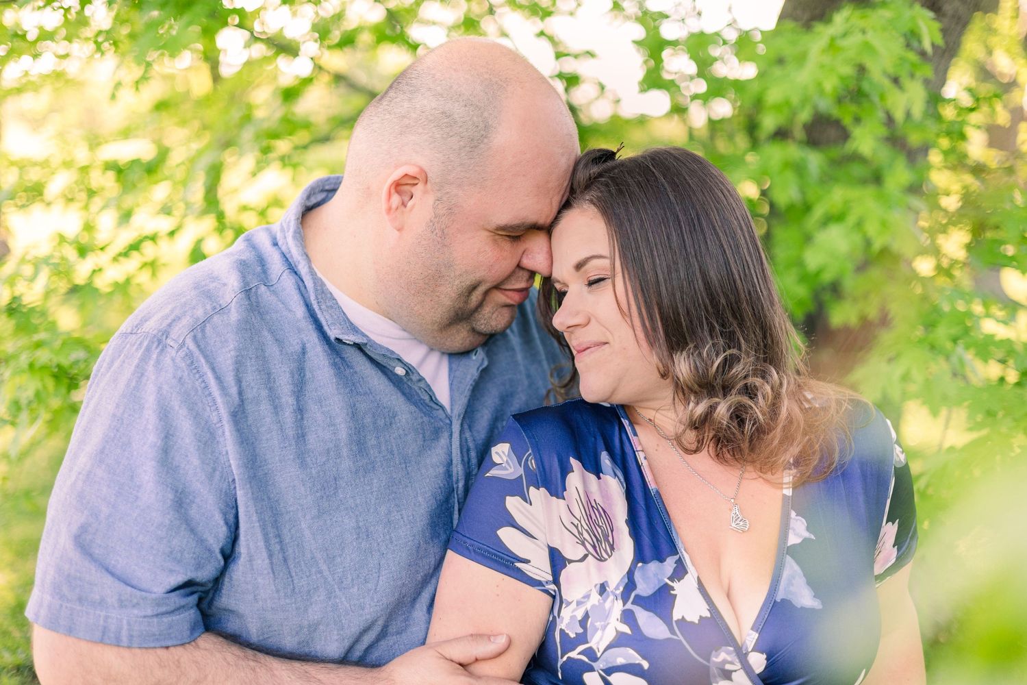 Intimate couple portrait in soft natural lighting with green foliage backdrop.