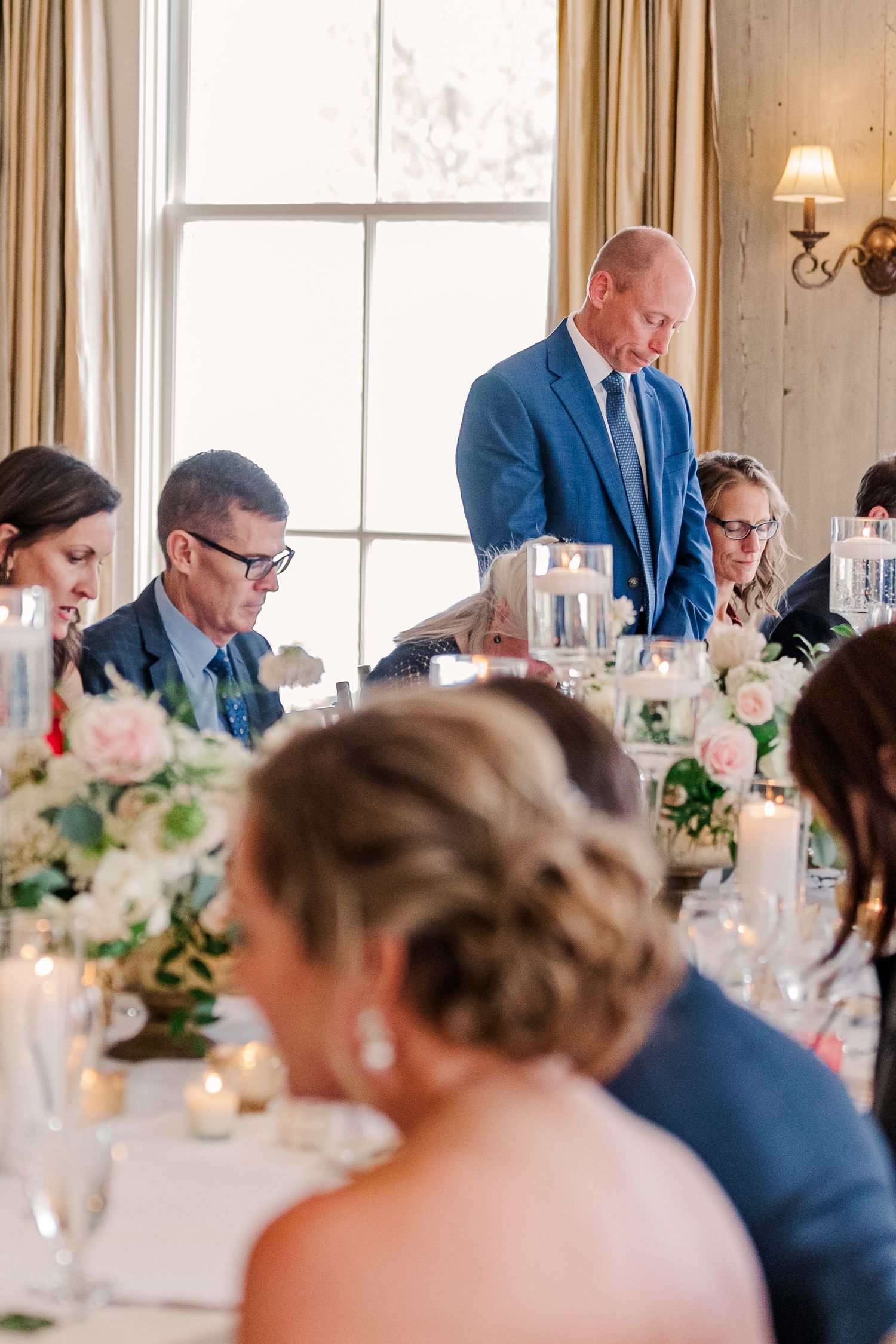 Reception dinner scene with elegant table settings, floral centerpieces and cream-colored curtains.