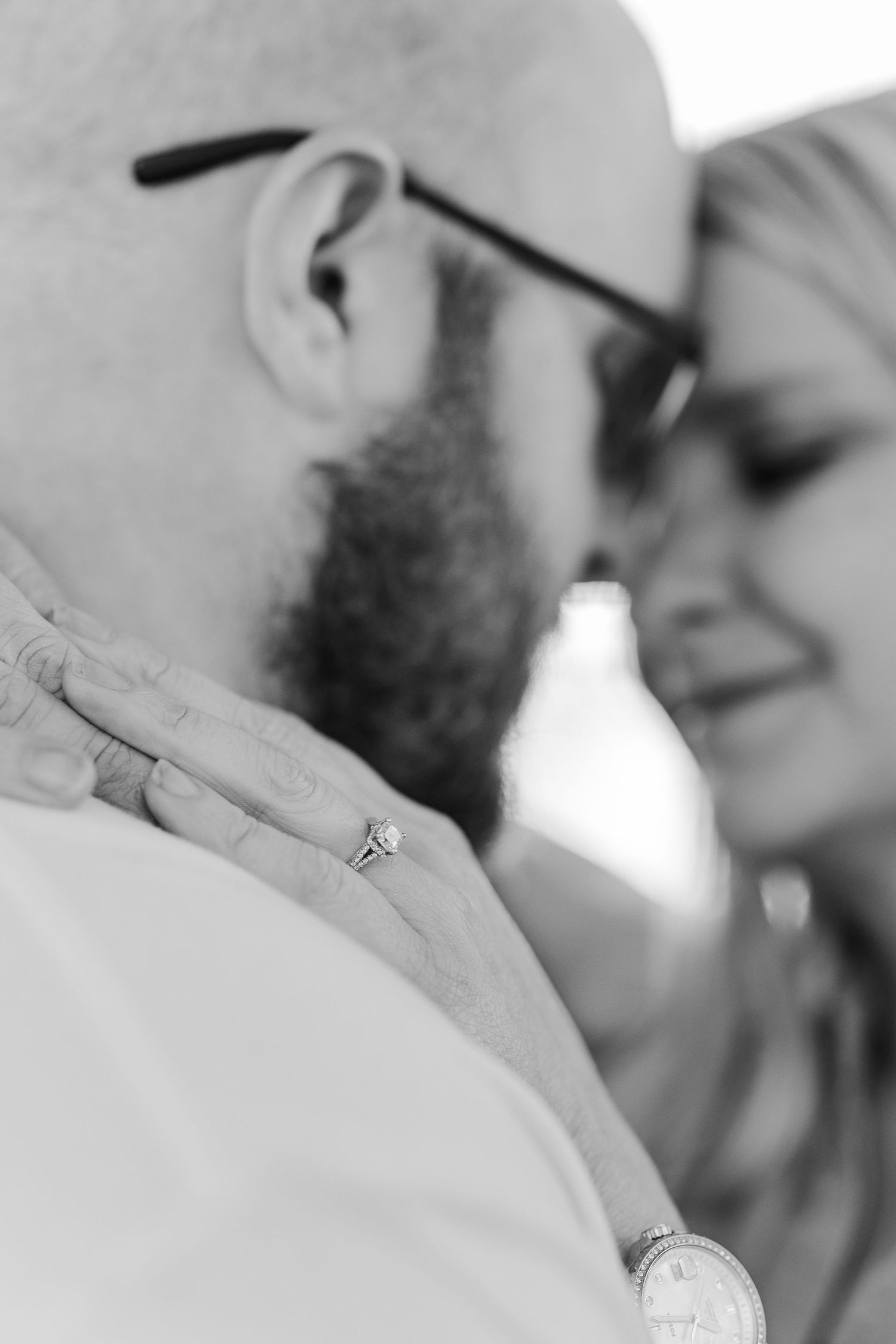 An intimate black and white close-up showing a ring and tender moment between a couple.