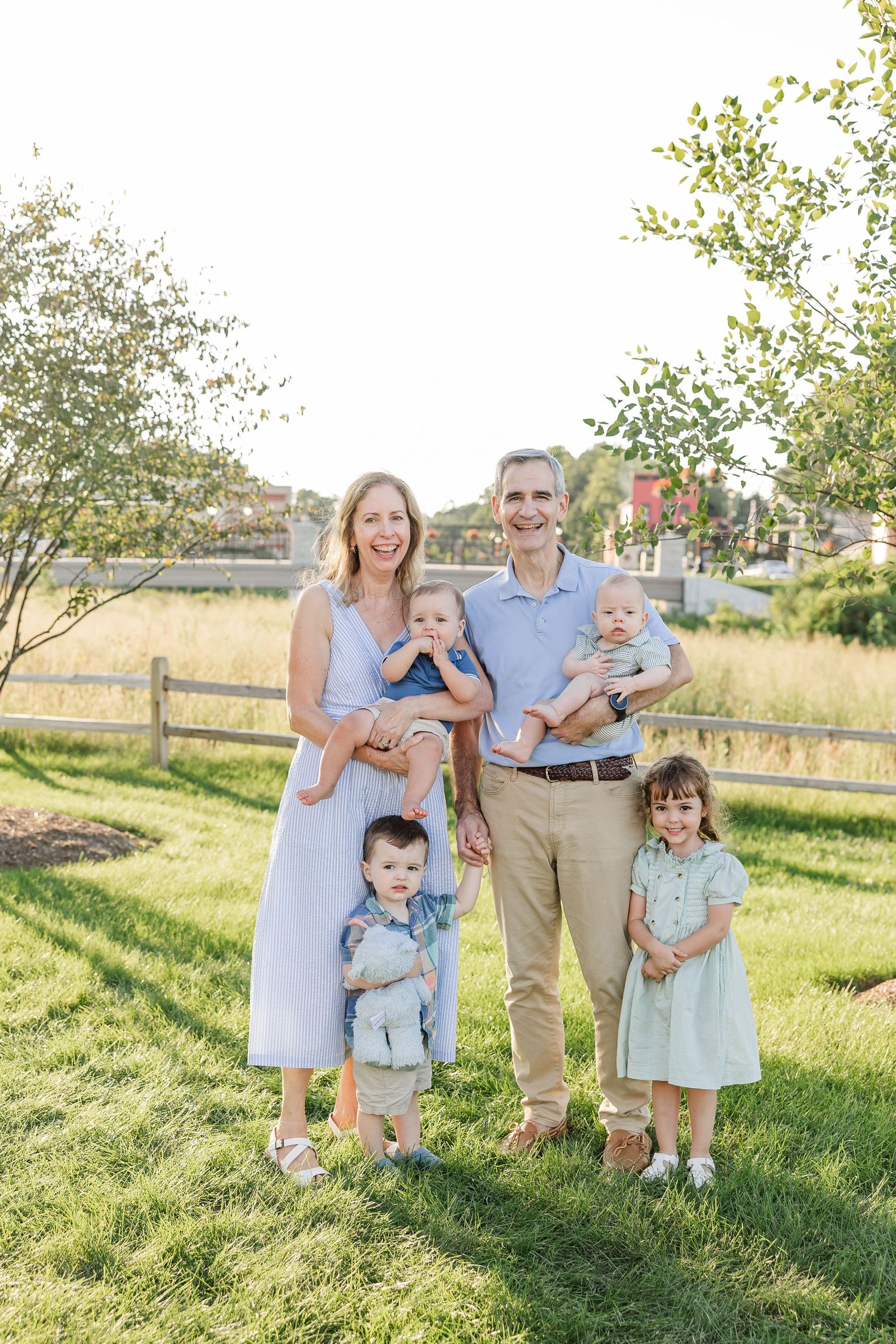 A cheerful family of five with three young children poses together on green grass in warm golden light.