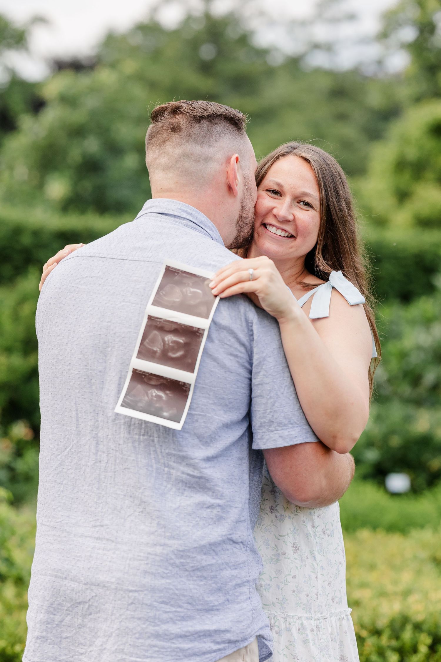 Expecting parents smiling together while holding ultrasound photos in the garden