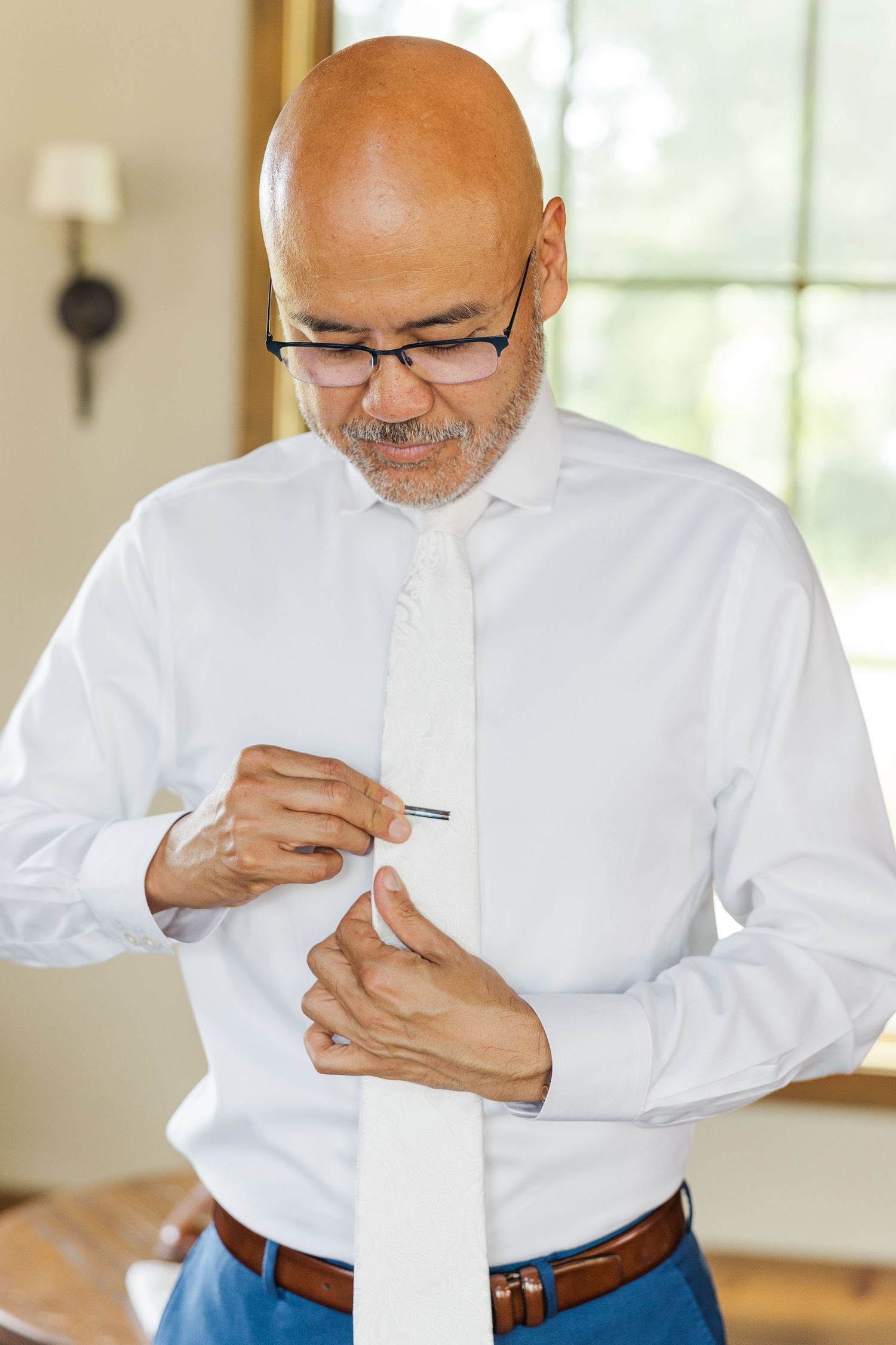 Person in white dress shirt and tie adjusting formal attire while getting ready.