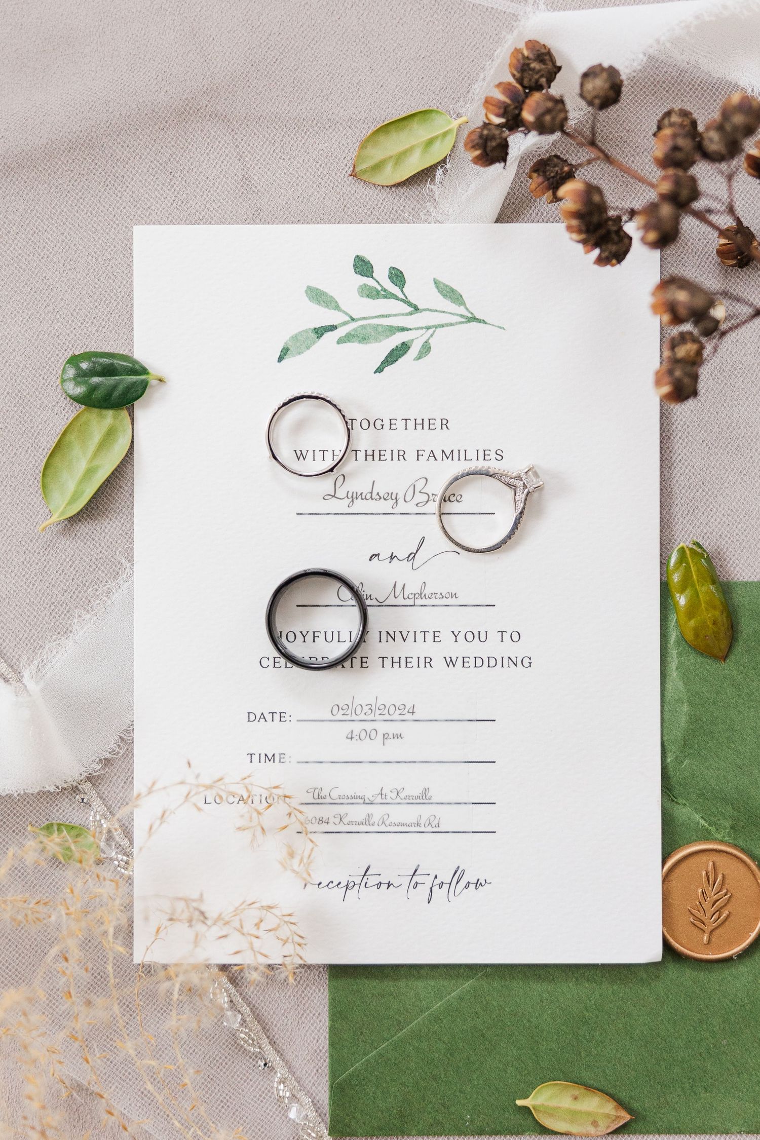 Wedding invitation with rings and botanical design displayed among green leaves.