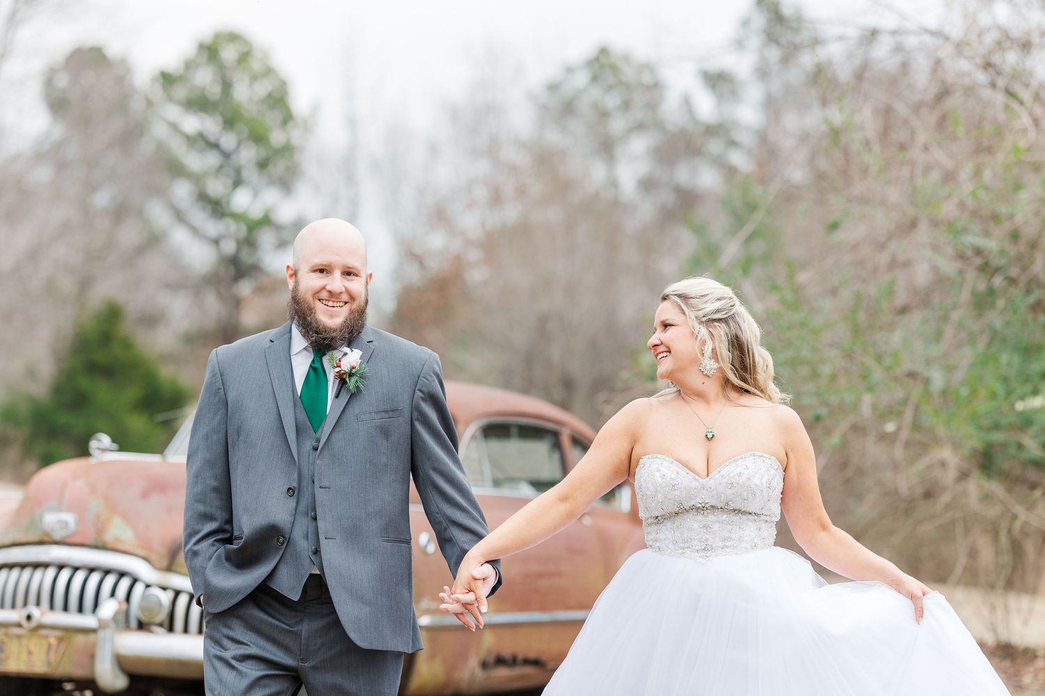 Wedding couple poses playfully in front of a classic rusty automobile.