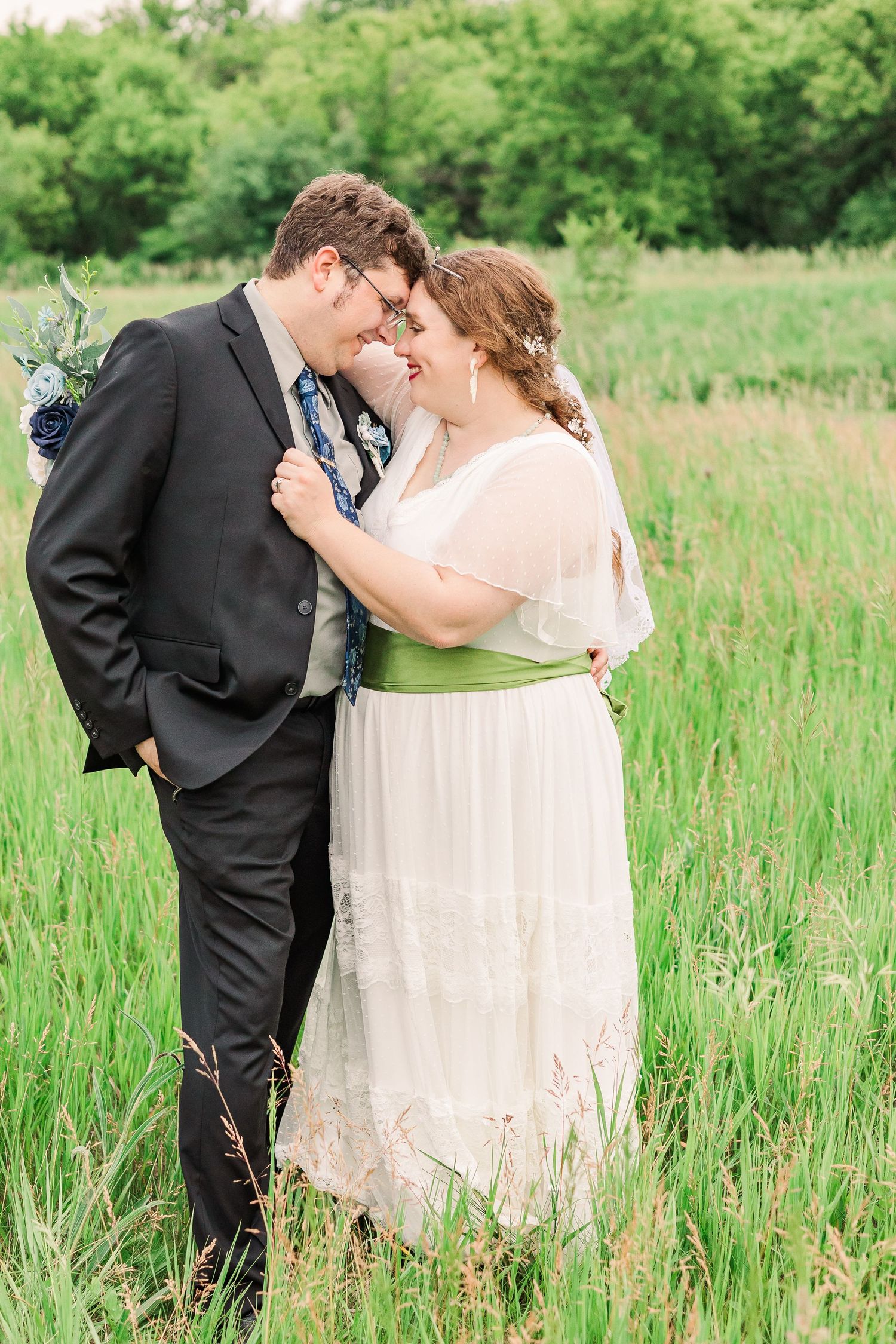A romantic wedding photo of a couple sharing an intimate moment in a green summer meadow.