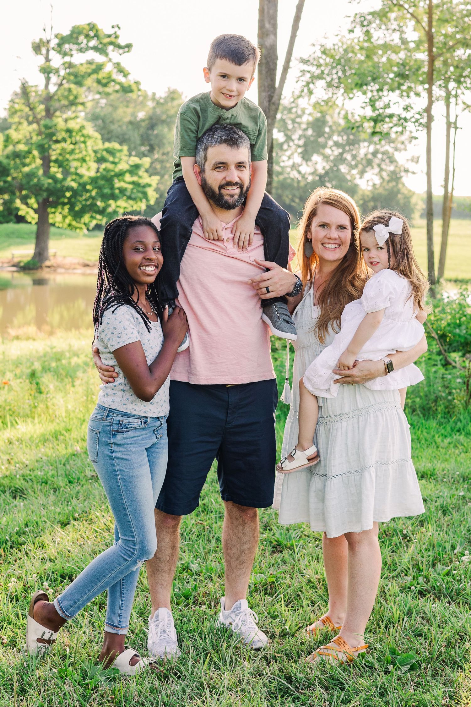 A happy family of five poses together on a sunny day in a park setting.
