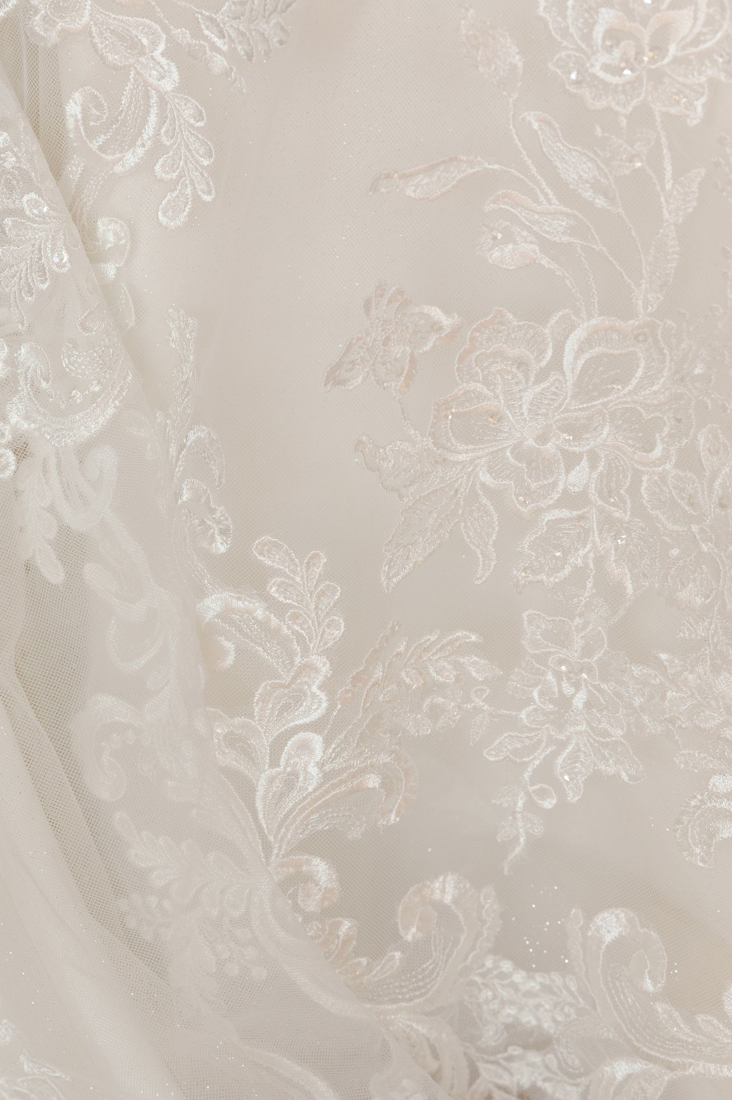 Close-up detail of delicate lace patterns on ivory wedding dress fabric.