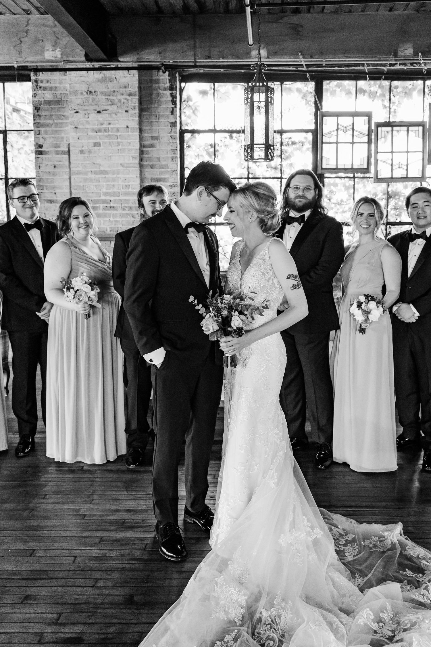 Intimate black and white wedding moment captured in industrial venue with bridal party looking on.