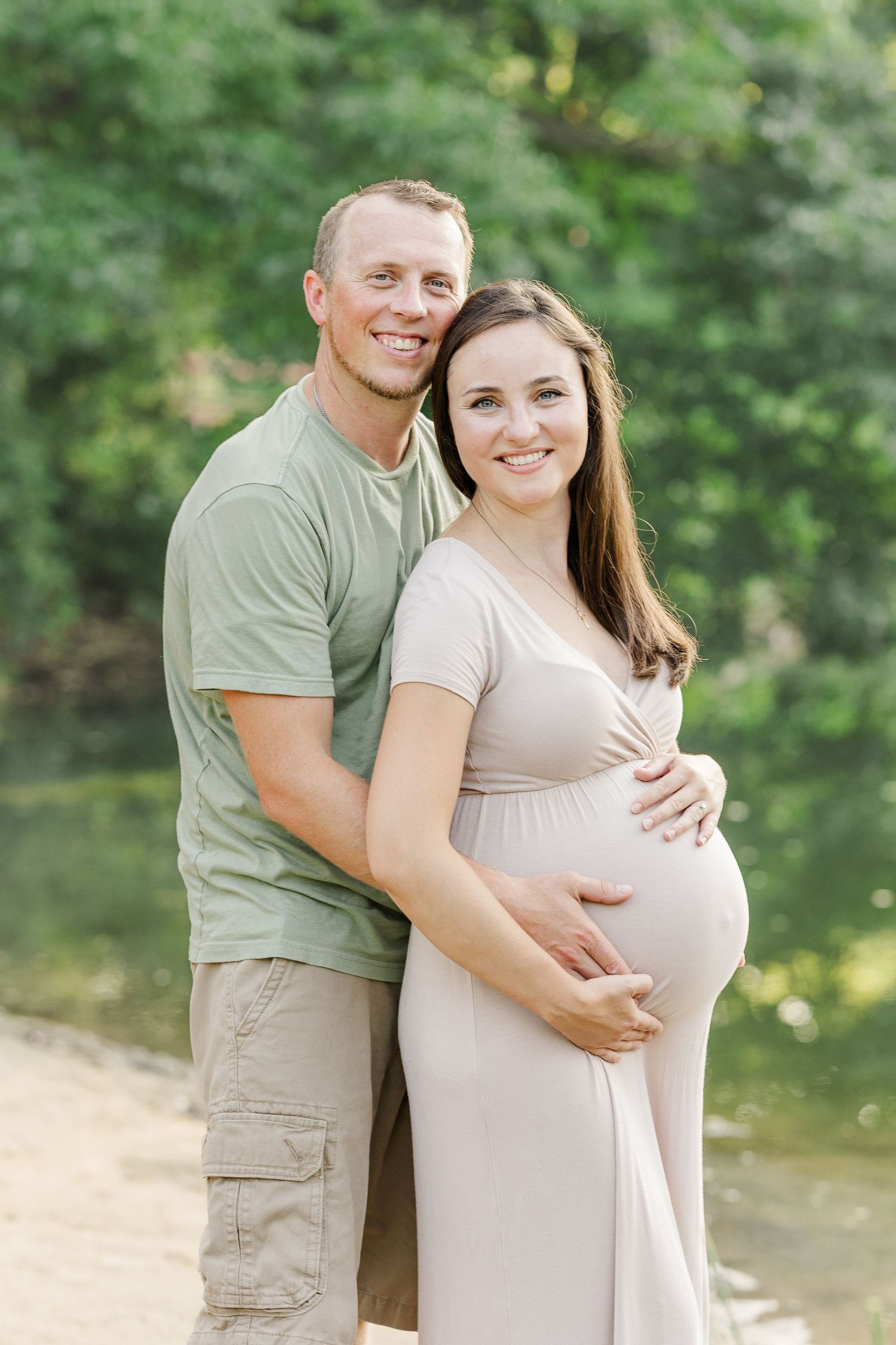 A couple in casual attire shares tender moments while posing outdoors against a lush green nature backdrop.