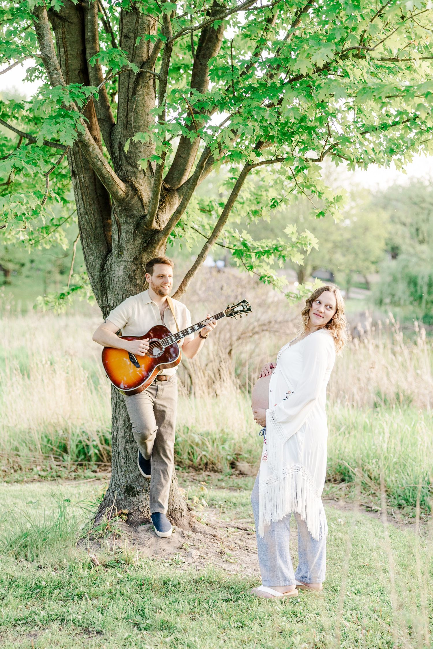 Father playing guitar for mother during a golden hour maternity session at Veterans Acres.
