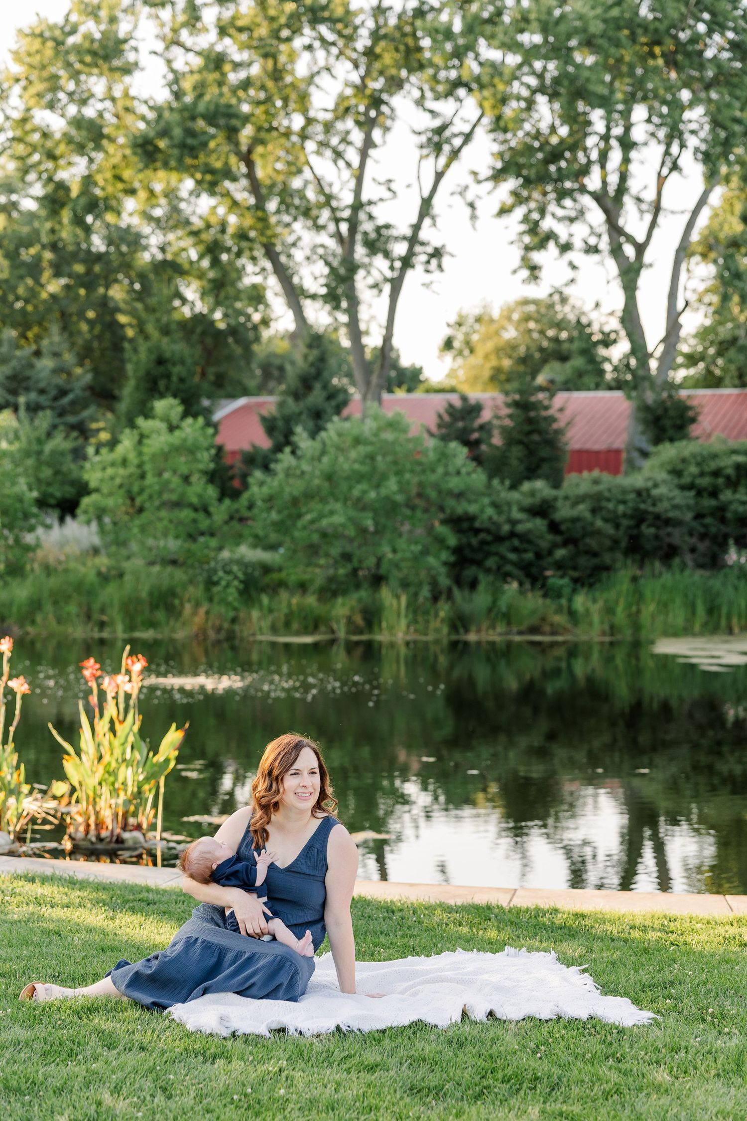 Hilary sitting with baby Lincoln on a blanket beside the peaceful pond at Cantigny Park.