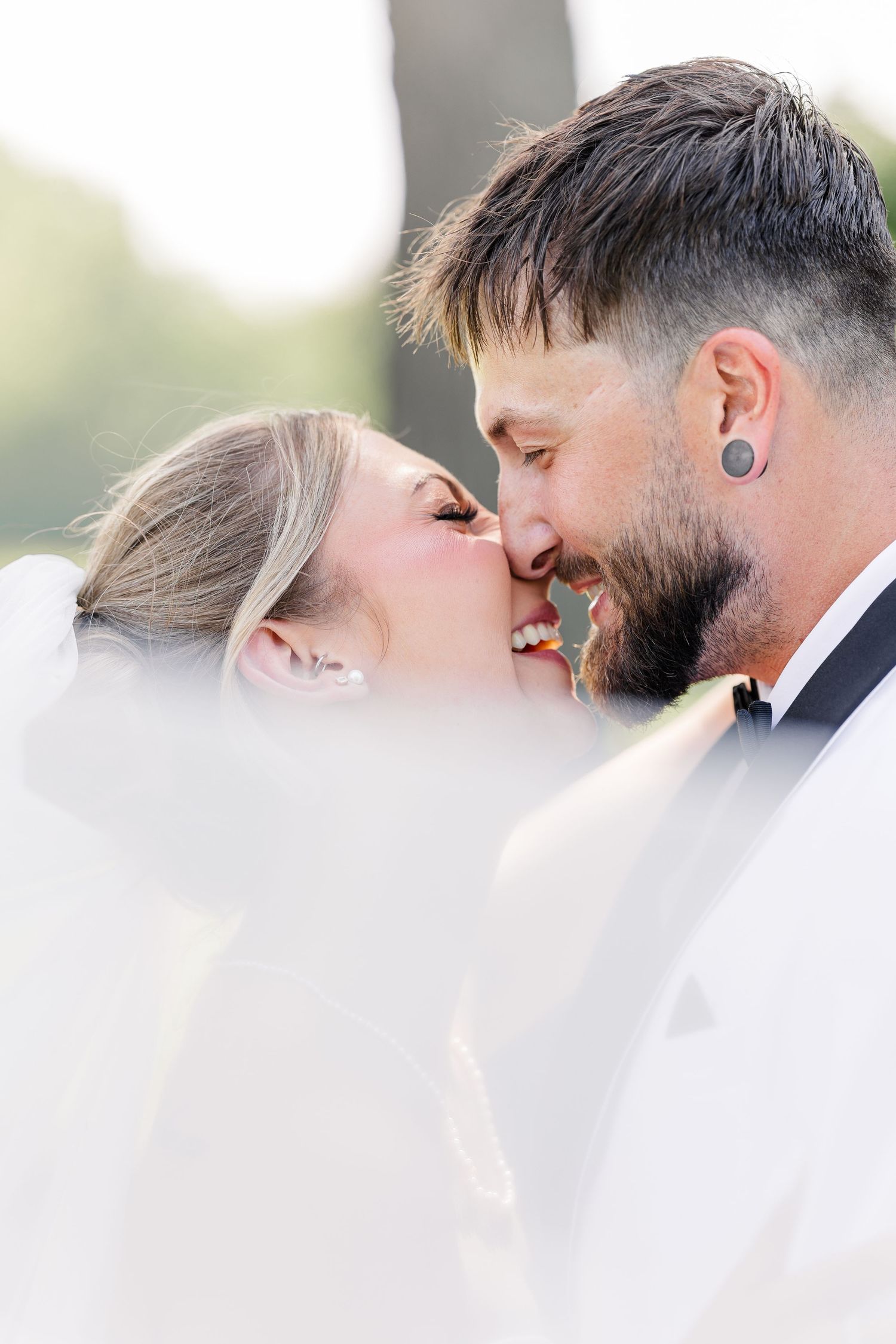 Bride and groom sharing romantic almost-kiss moment wrapped in flowing white veil outdoors.