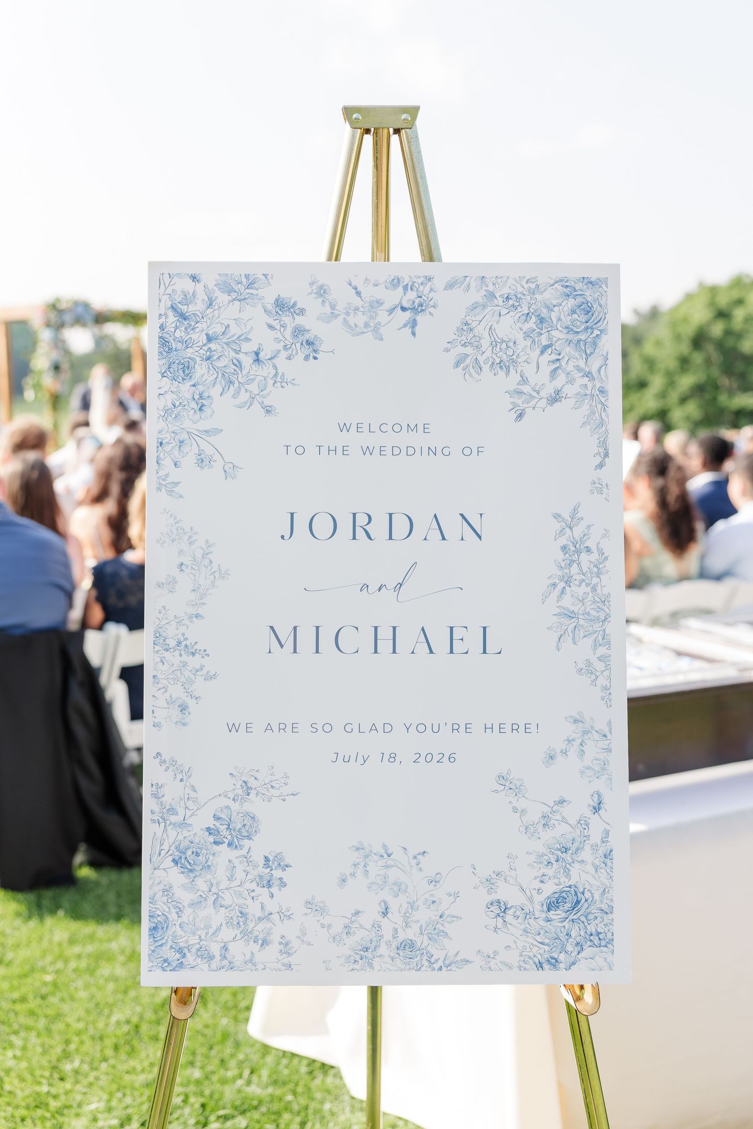 Elegant blue floral wedding welcome sign for Jordan and Michael on a gold easel, July 18 2026.