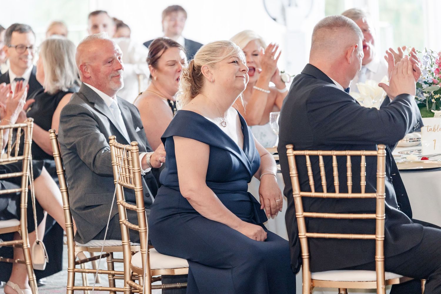 Wedding guests in formal attire applauding during reception at elegantly decorated venue.