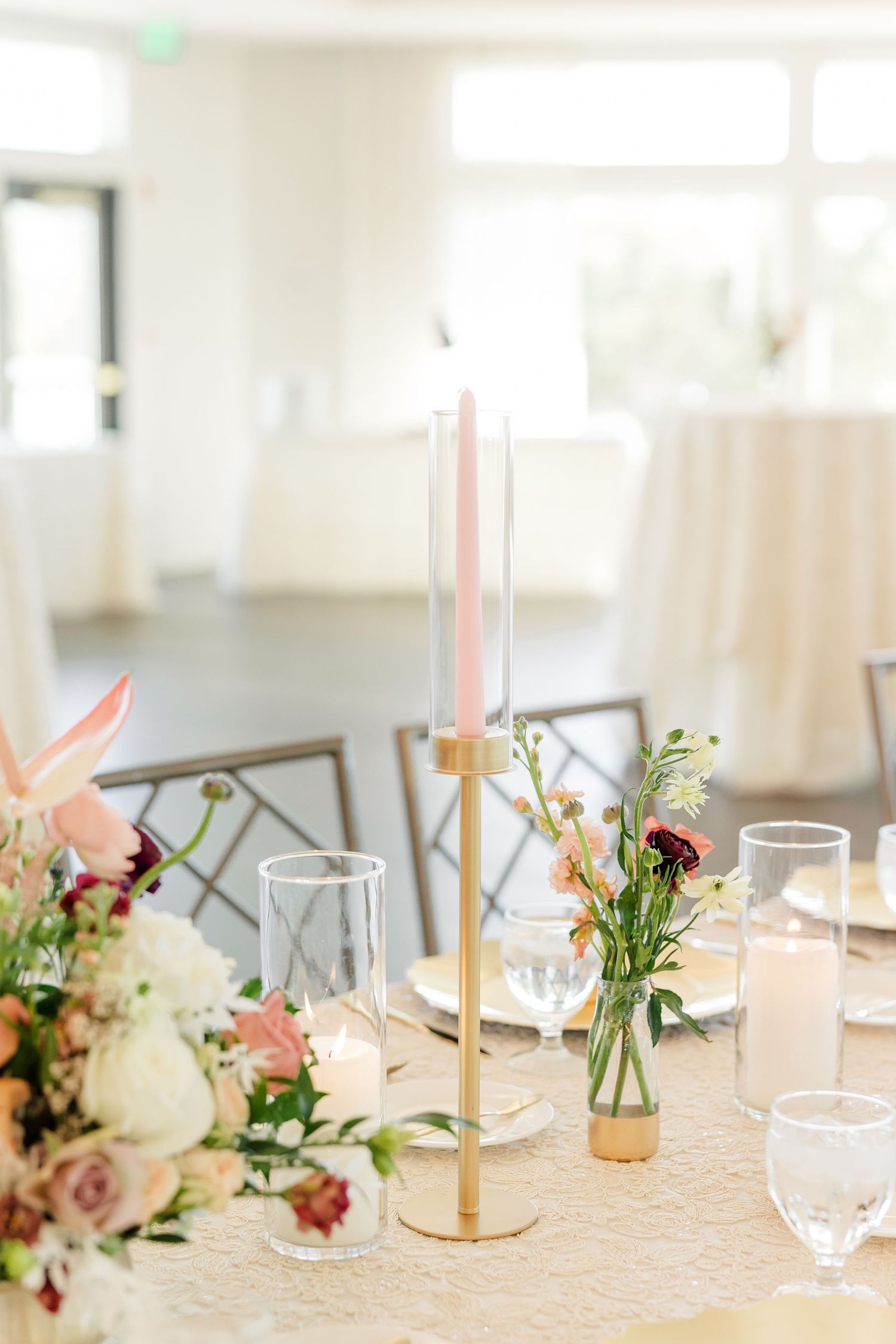 Elegant wedding reception table with a gold candlestick holder, pink taper candle, glass votives, and blush floral centerpieces.