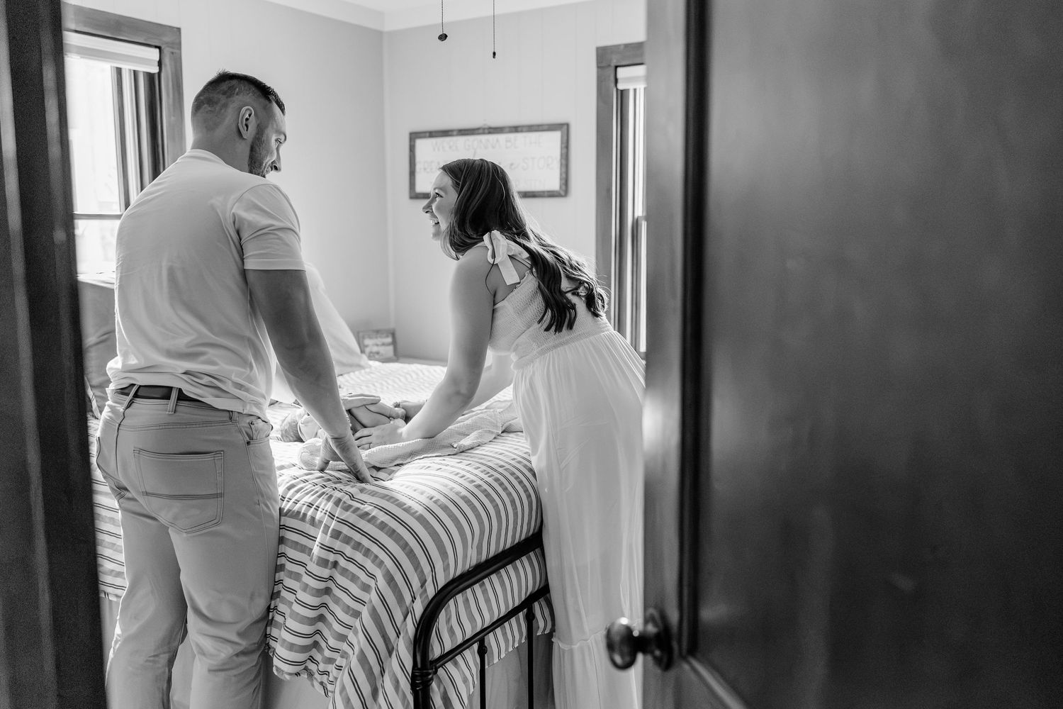 Couple holding hands beside a bed in a softly lit bedroom in black and white.