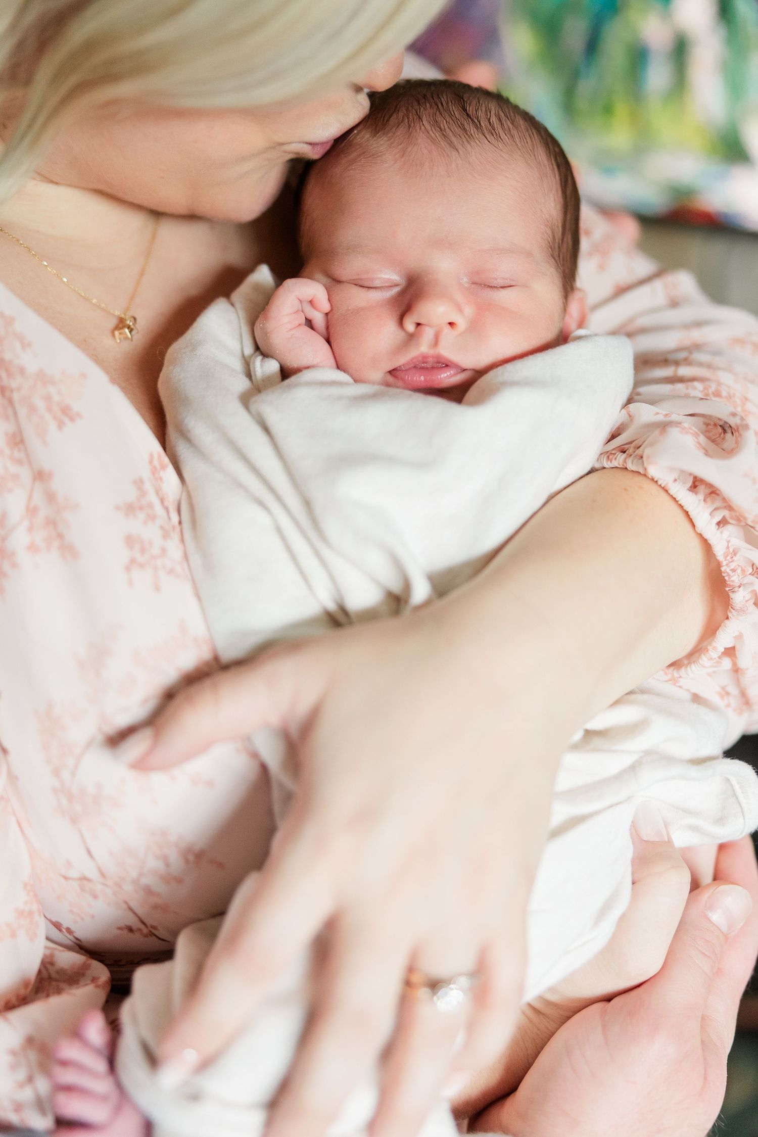 A mother in a floral dress gently holds her sleeping newborn baby close to her face.
