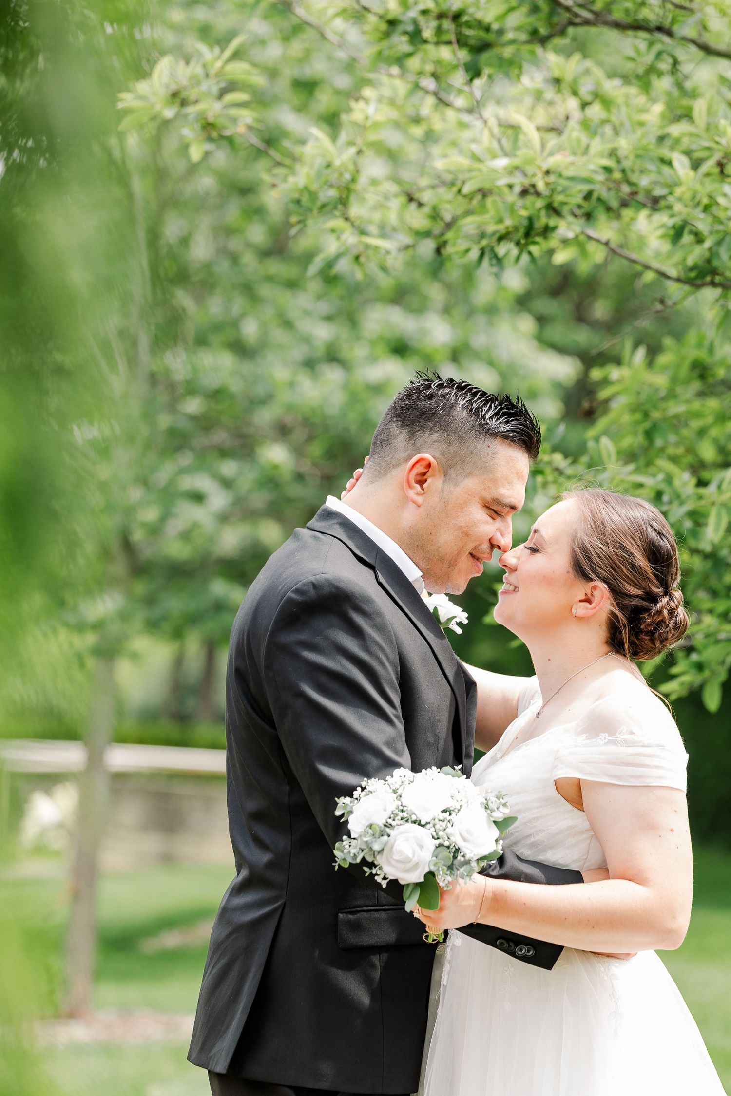Monika and Rafael smiling at one another beneath the trees during their newlywed portrait session.
