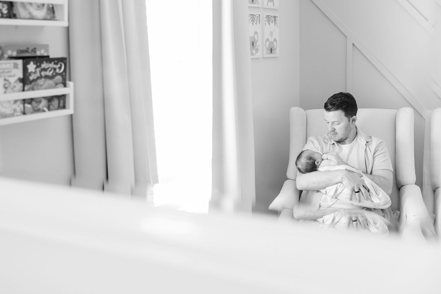 Black and white nursery photo of dad holding newborn baby girl during an in-home lifestyle session