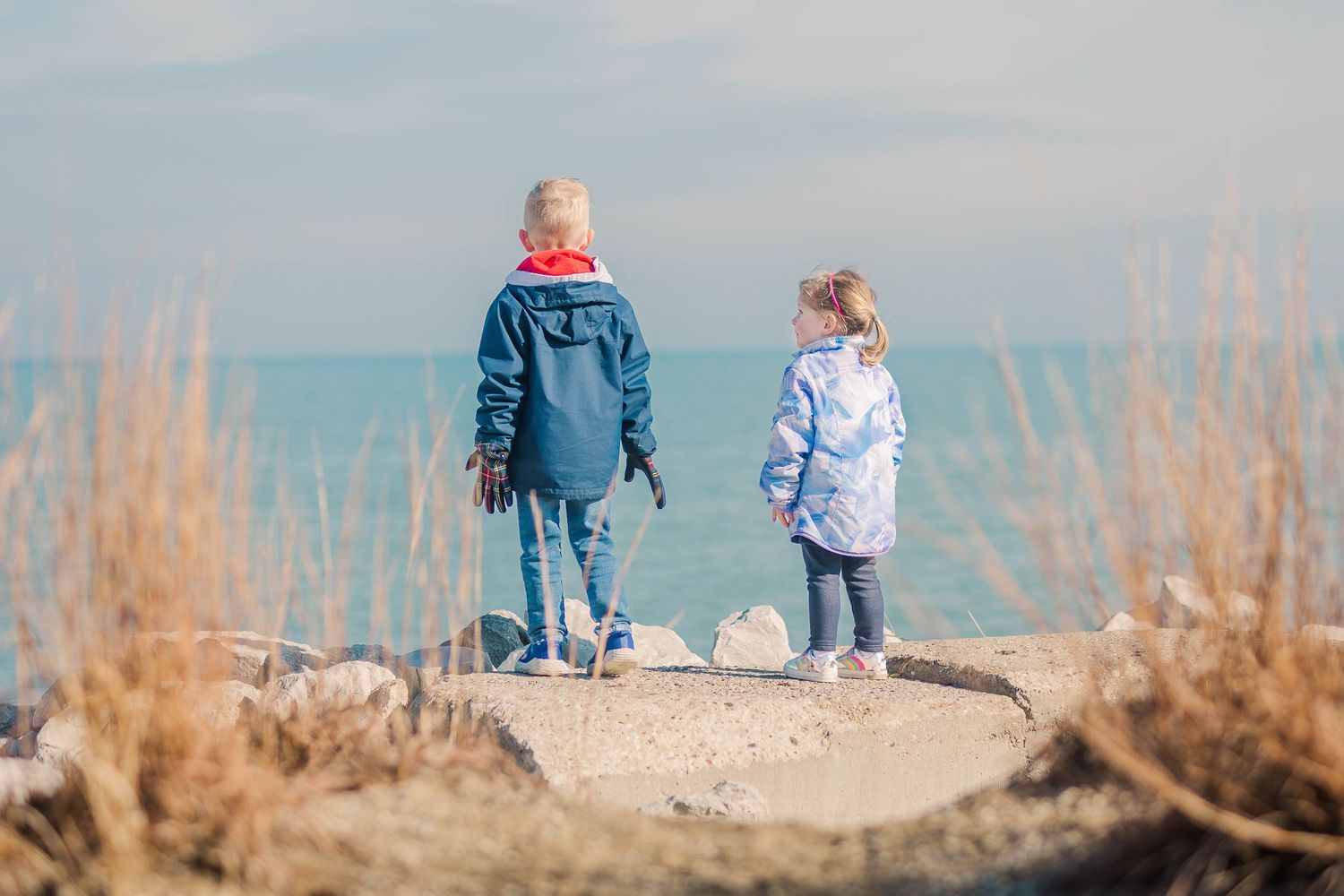 Two people enjoying a walk along a coastal path lined with dried beach grass.