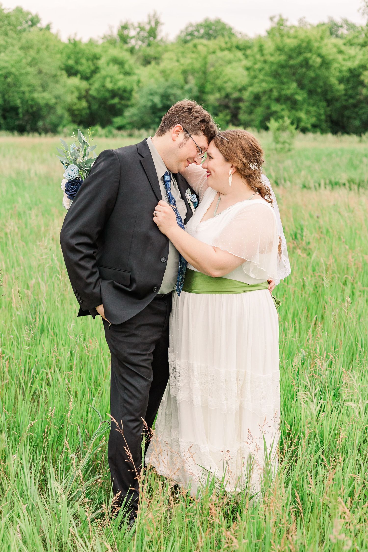 A romantic wedding portrait showing the couple embracing in tall summer grass.