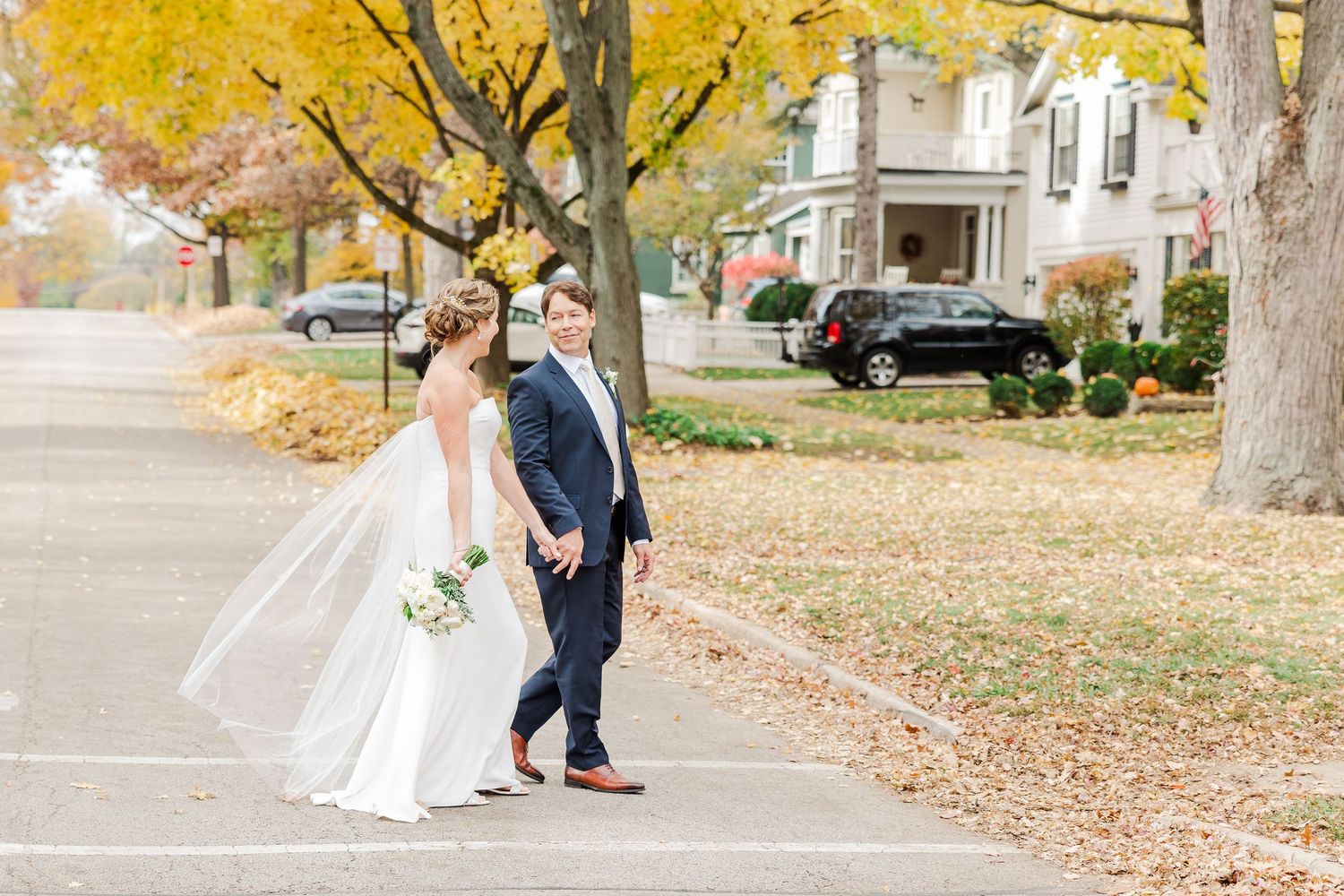Autumn wedding photo with couple walking on street lined with golden trees.