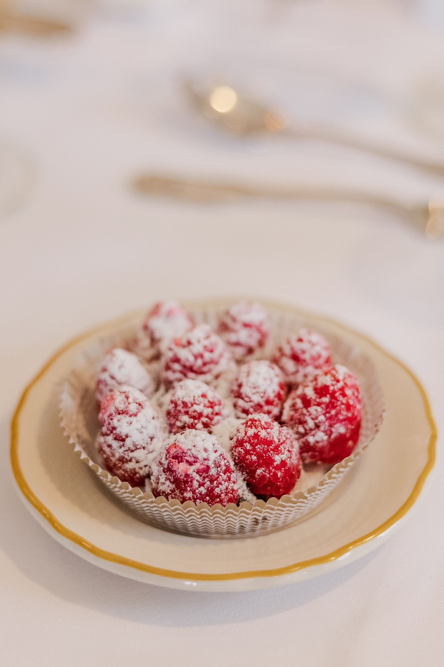Fresh red raspberries dusted with powdered sugar served on an elegant gold-rimmed plate.