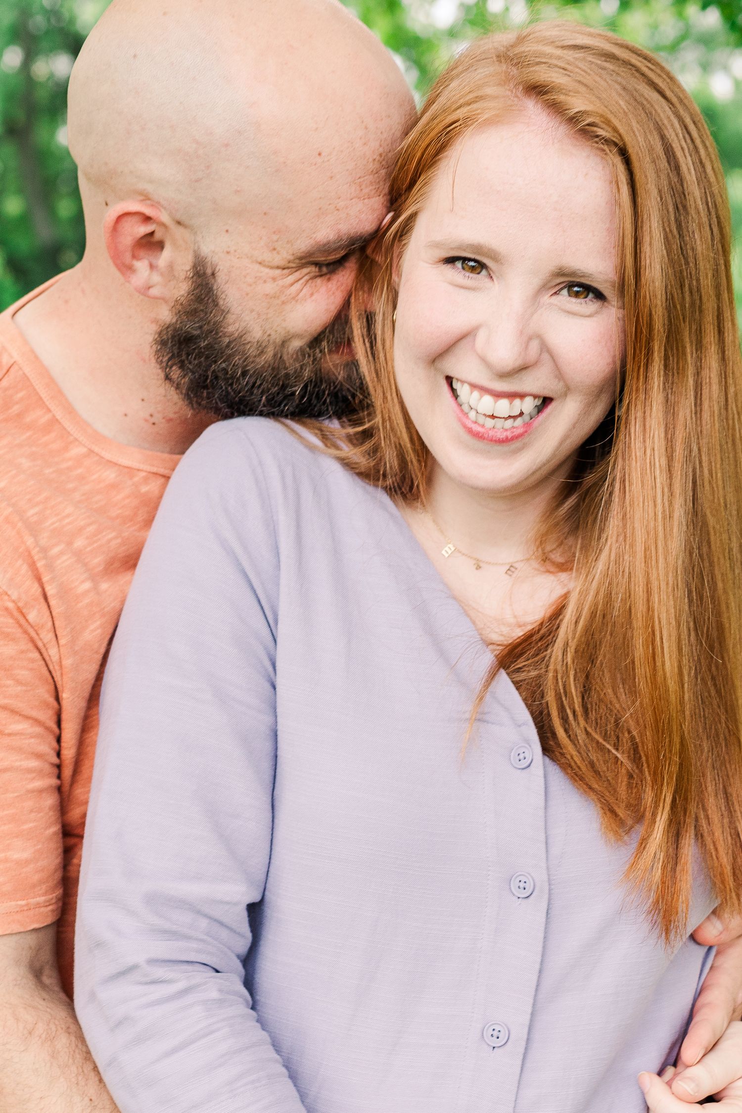 A tender moment captured between a couple against a leafy green background in natural lighting.