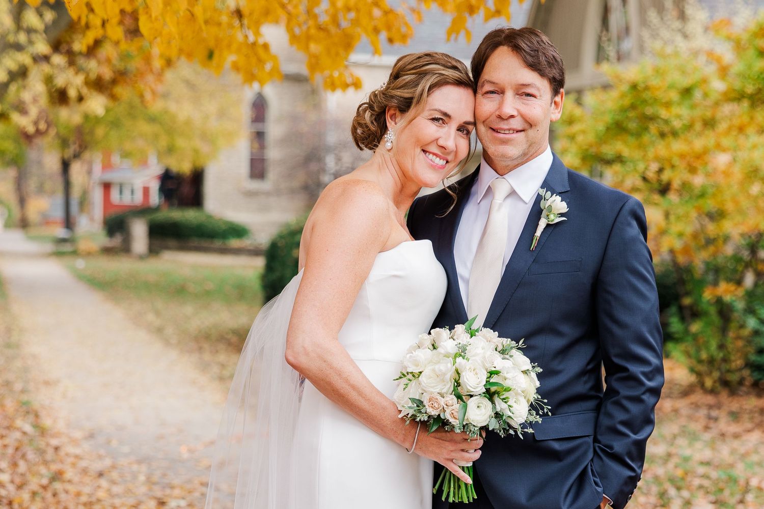 Autumn wedding portrait with couple against golden leaves and stone building.