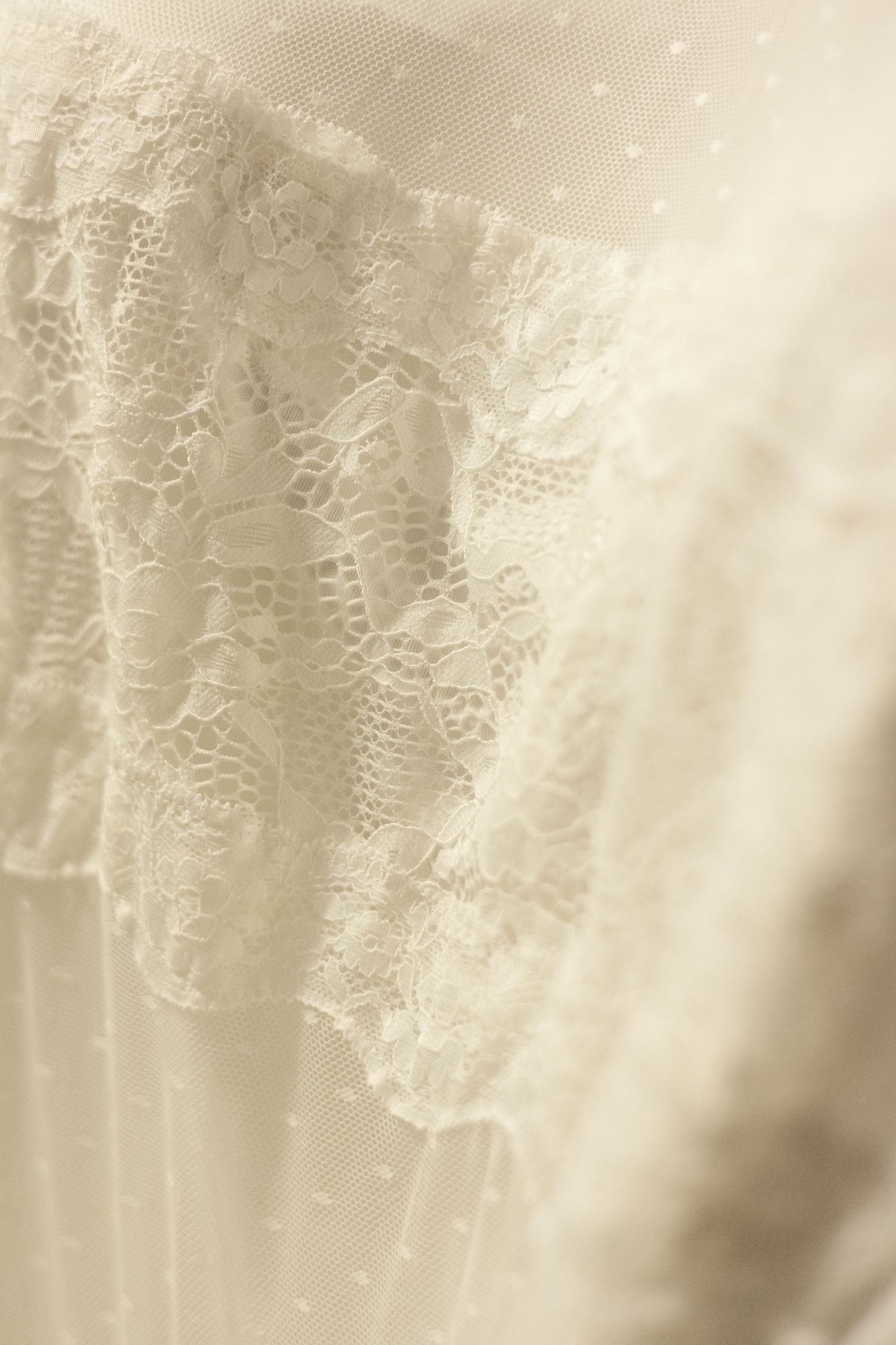 Delicate ivory lace detail on flowing fabric with soft lighting.