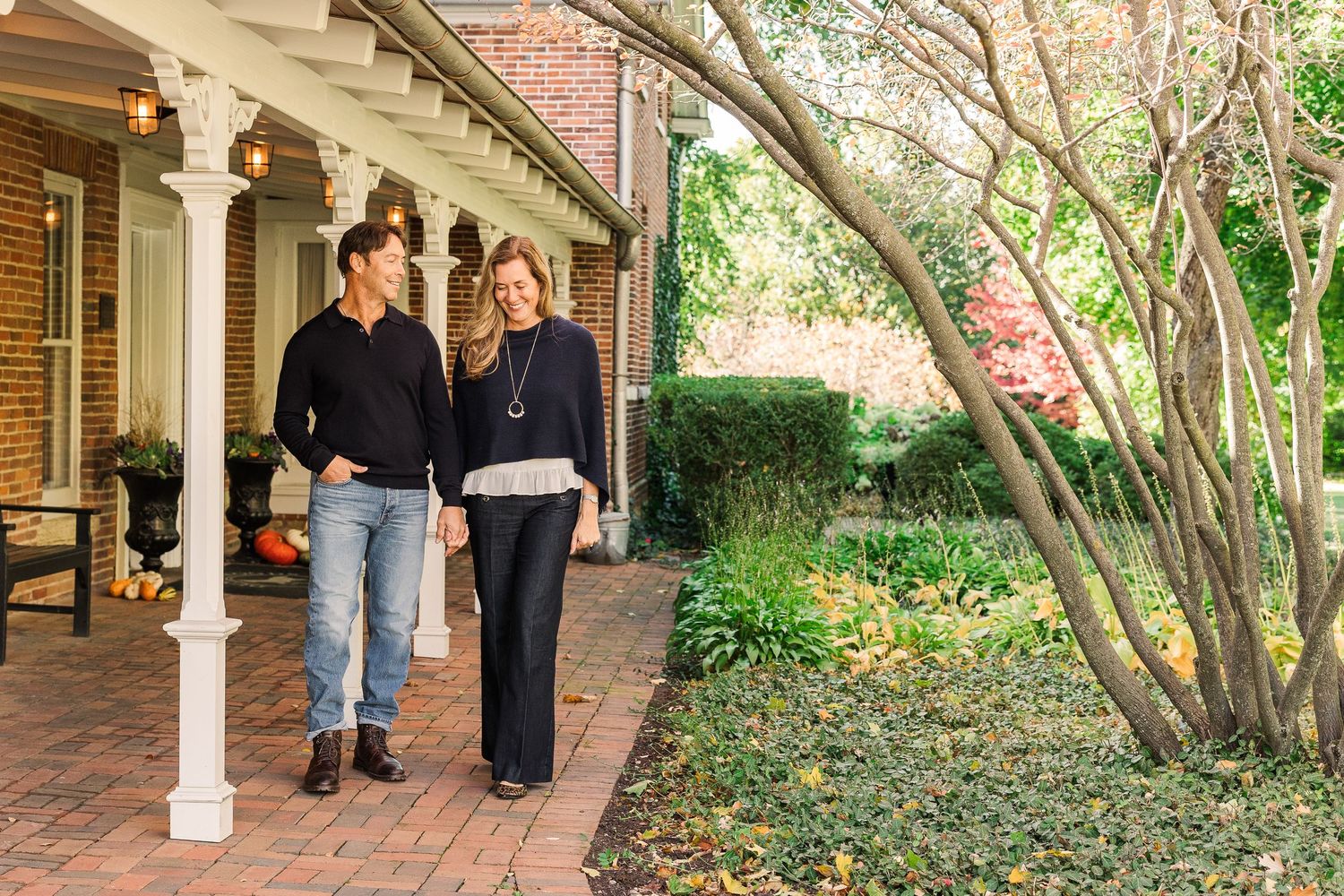 Couple walking together on brick path beside autumn foliage and garden.