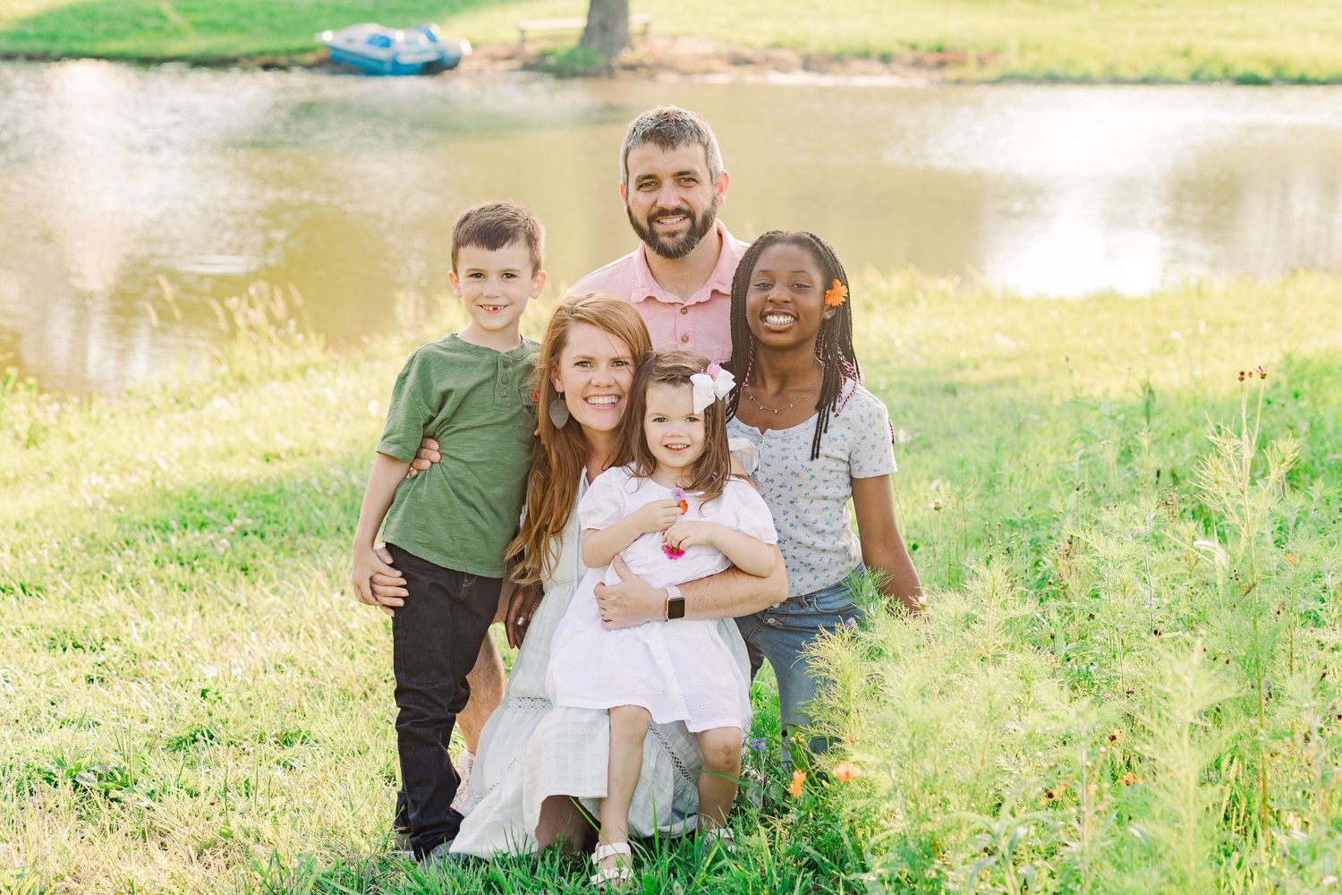 Family members gather close for a casual outdoor portrait by a pond.