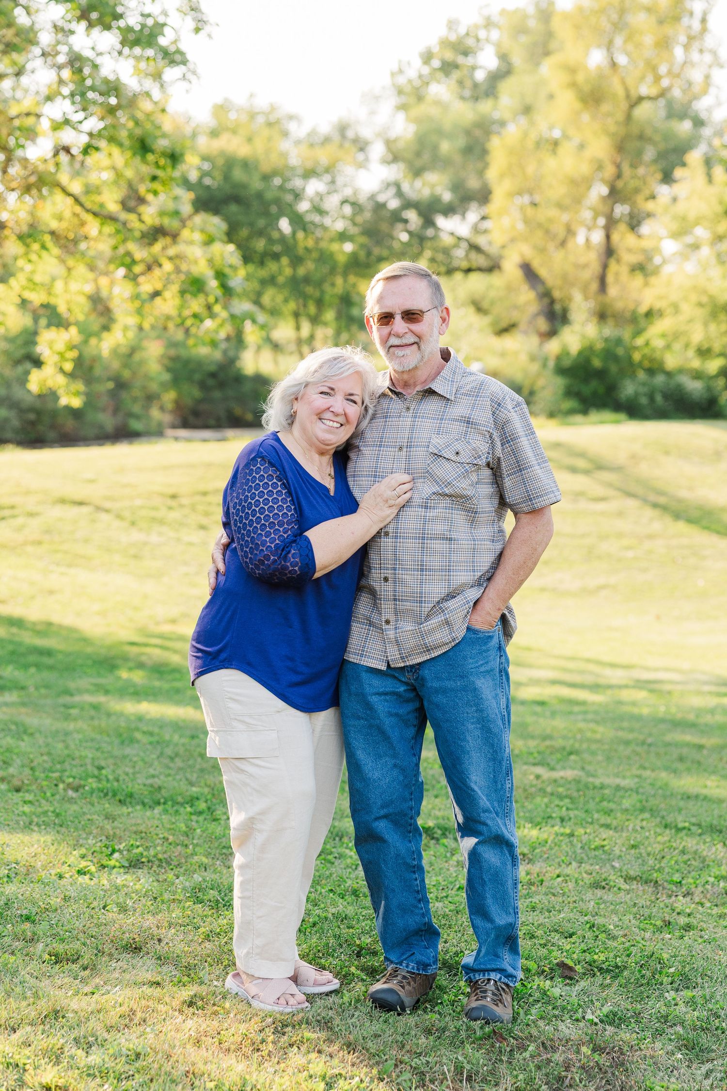 An older couple shares a joyful embrace while standing together on a grassy hillside on a sunny autumn day.Sorg family portraits at Shamrock