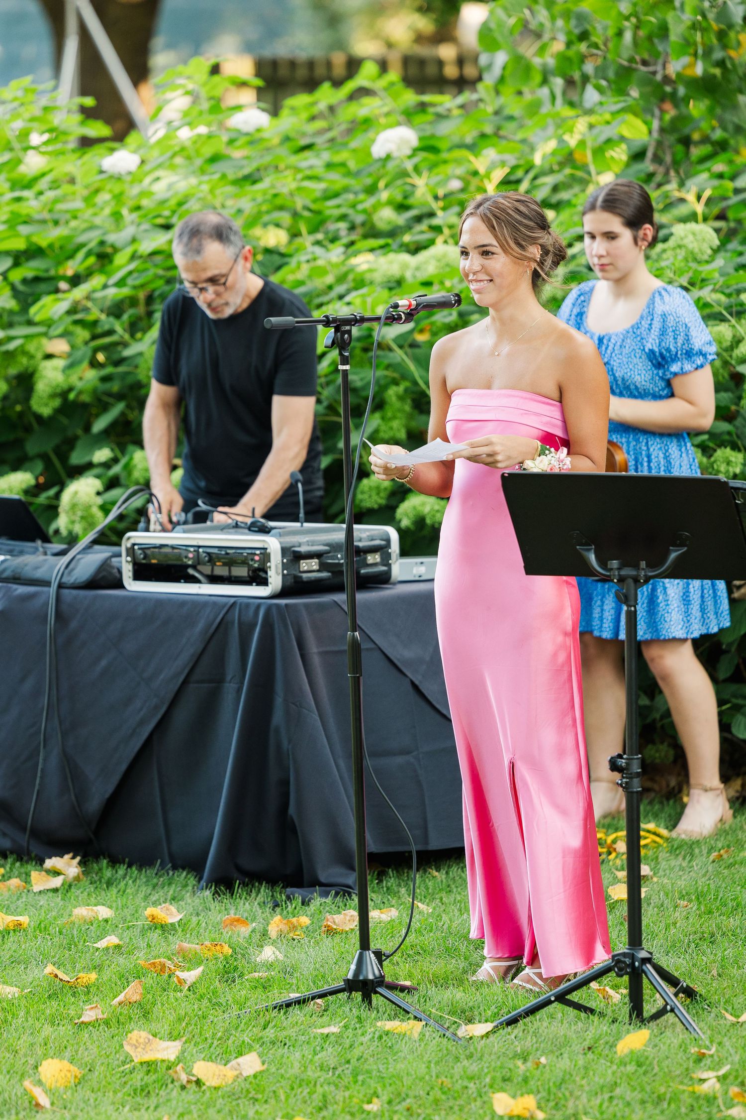 Performers setting up for outdoor event with DJ equipment and microphone stands on black table.