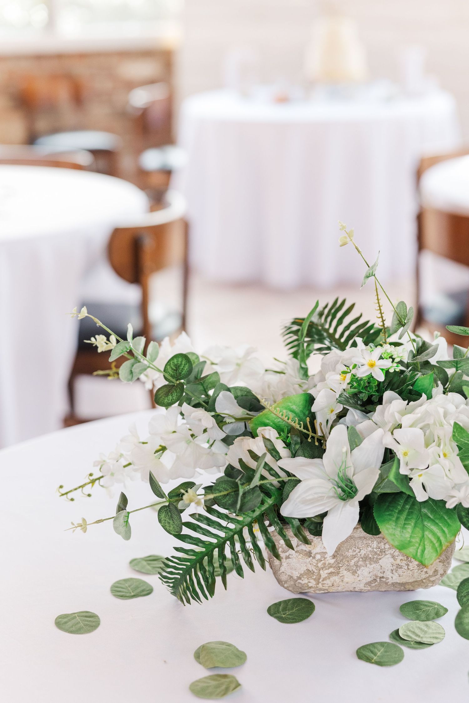 White floral and greenery centerpiece arrangement with silver eucalyptus leaves on reception table.