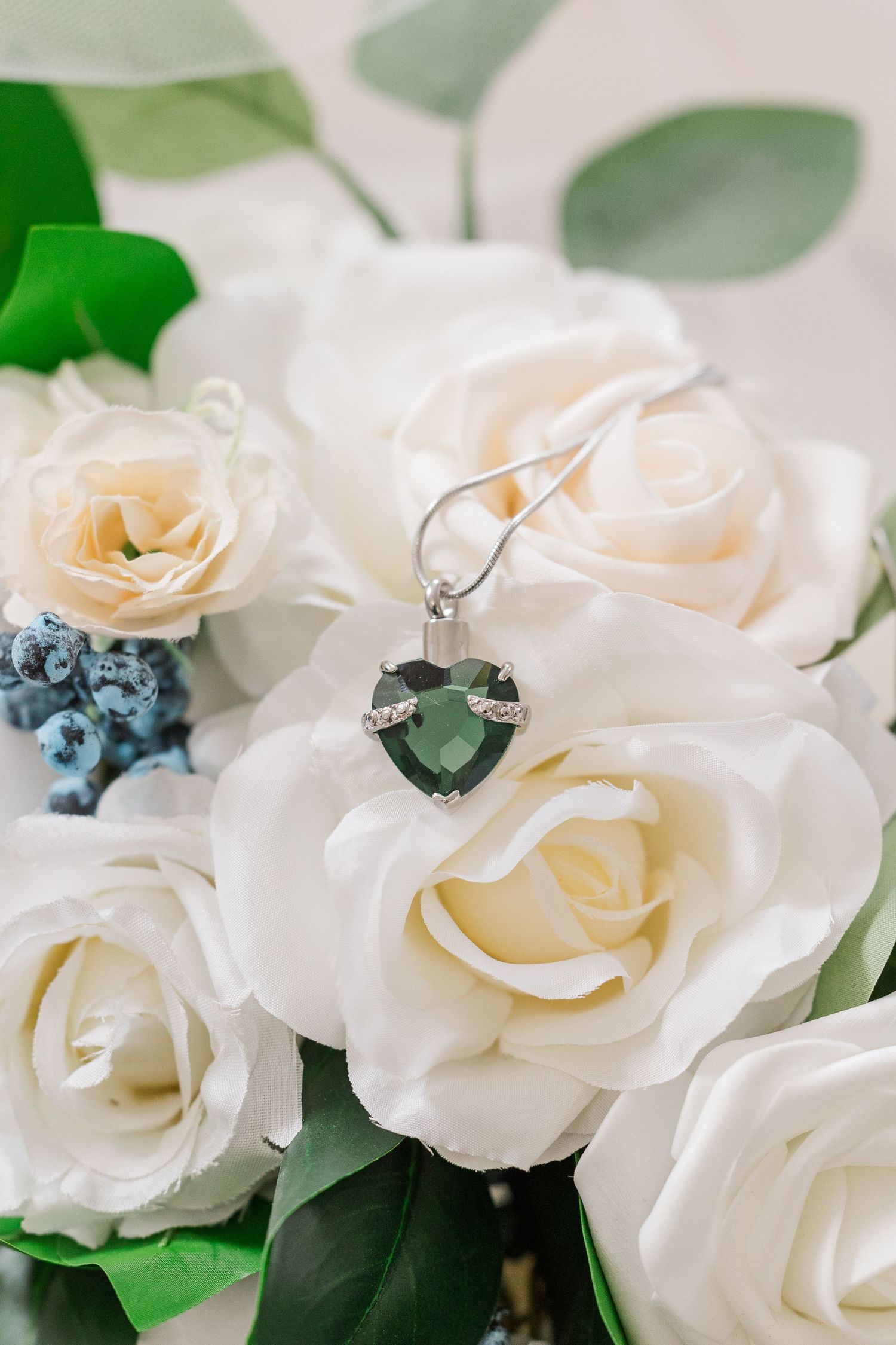 Heart-shaped gemstone pendant displayed on white roses with green foliage.