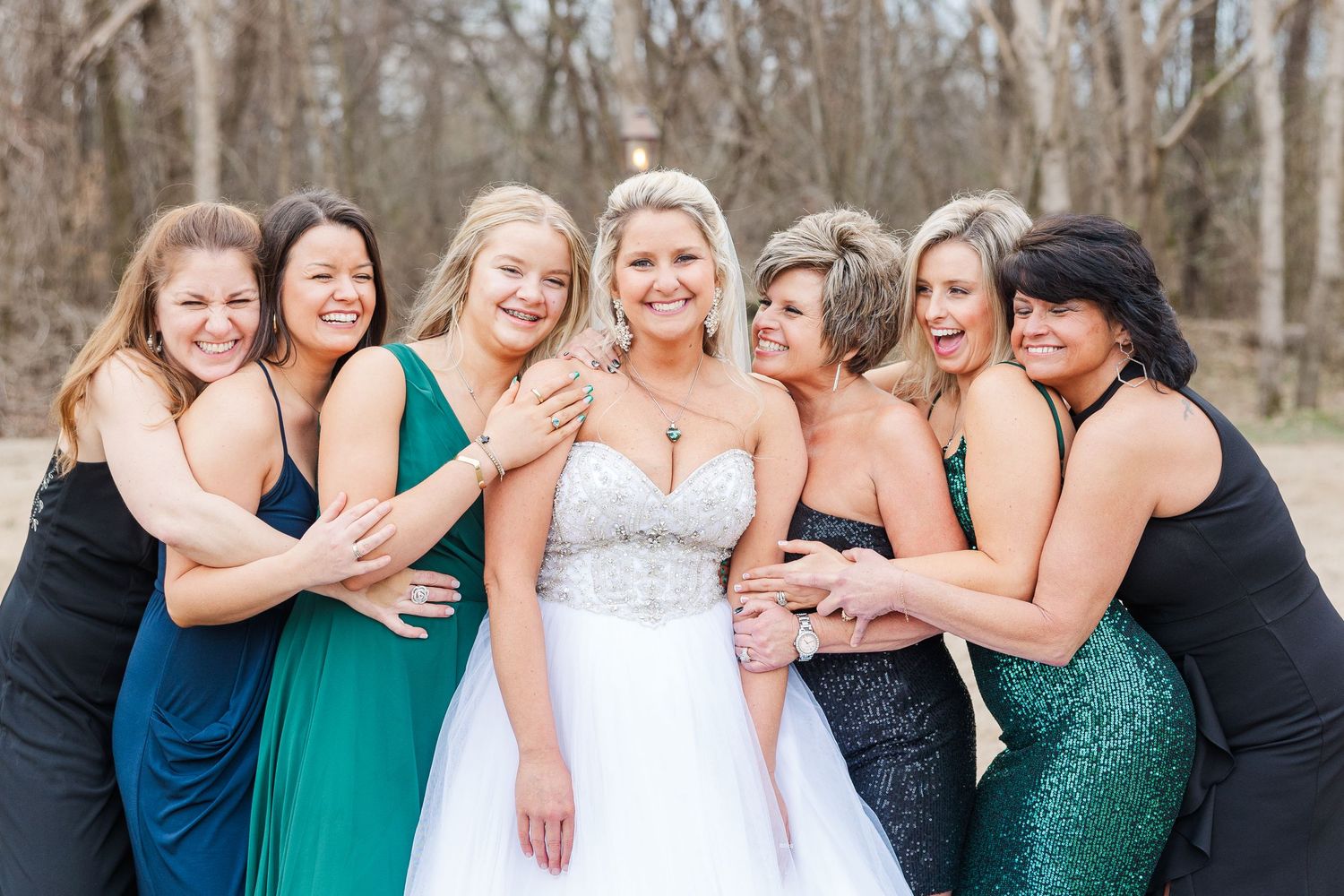 Bridesmaids in stunning evening gowns embrace while sharing a joyful moment outdoors.