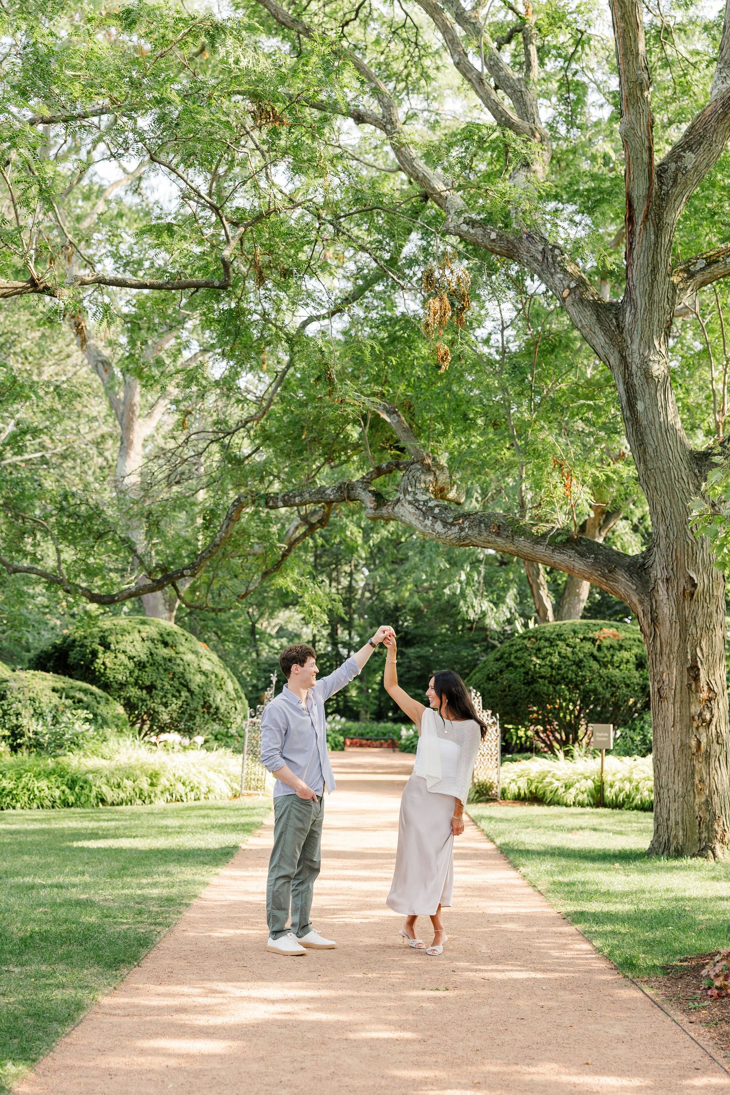 Alysia and Jack walk hand in hand along a tree-lined path at Cantigny Park.