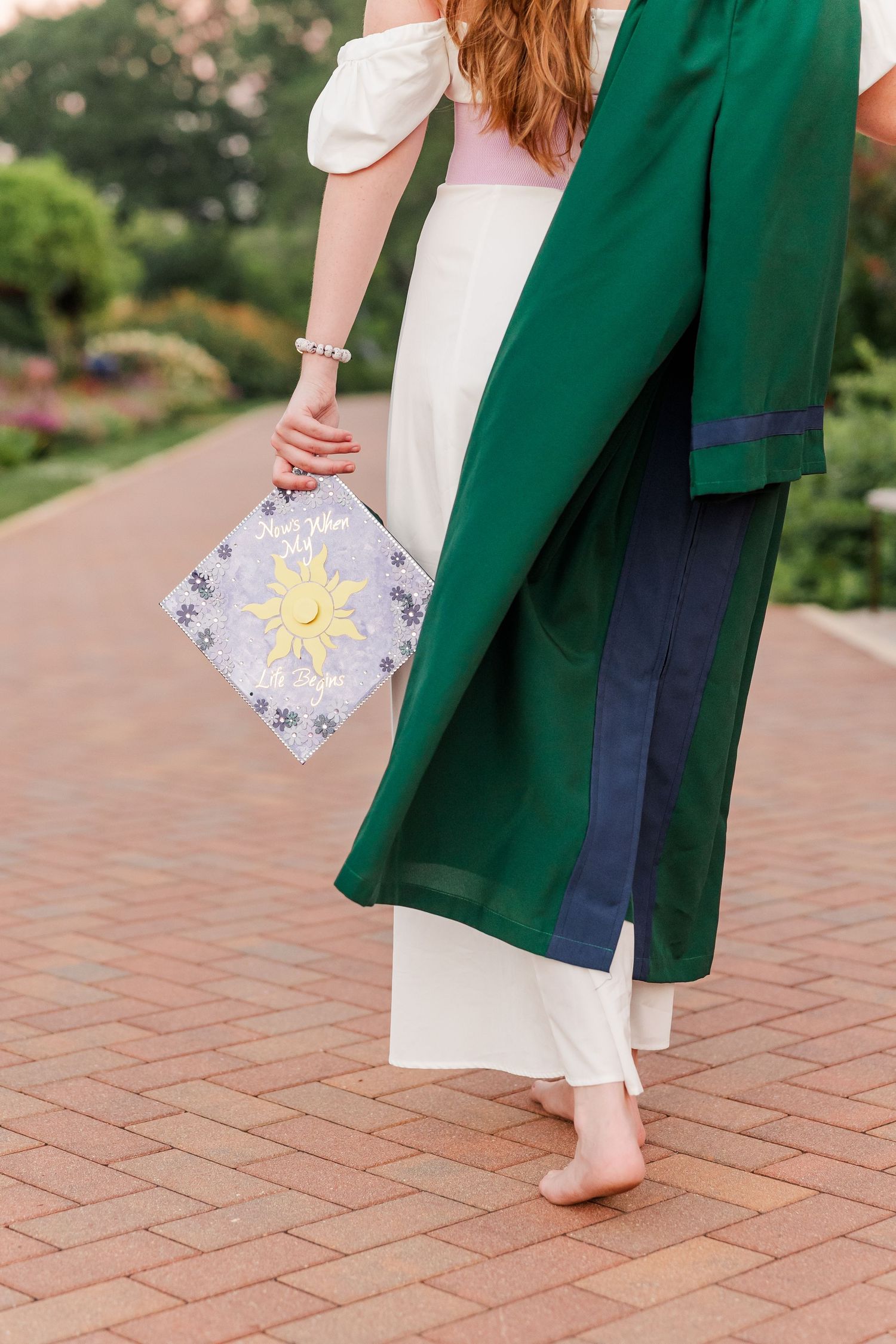 Detail of Samantha carrying her decorated graduation cap and green gown during her Class of 2027 senior session.
