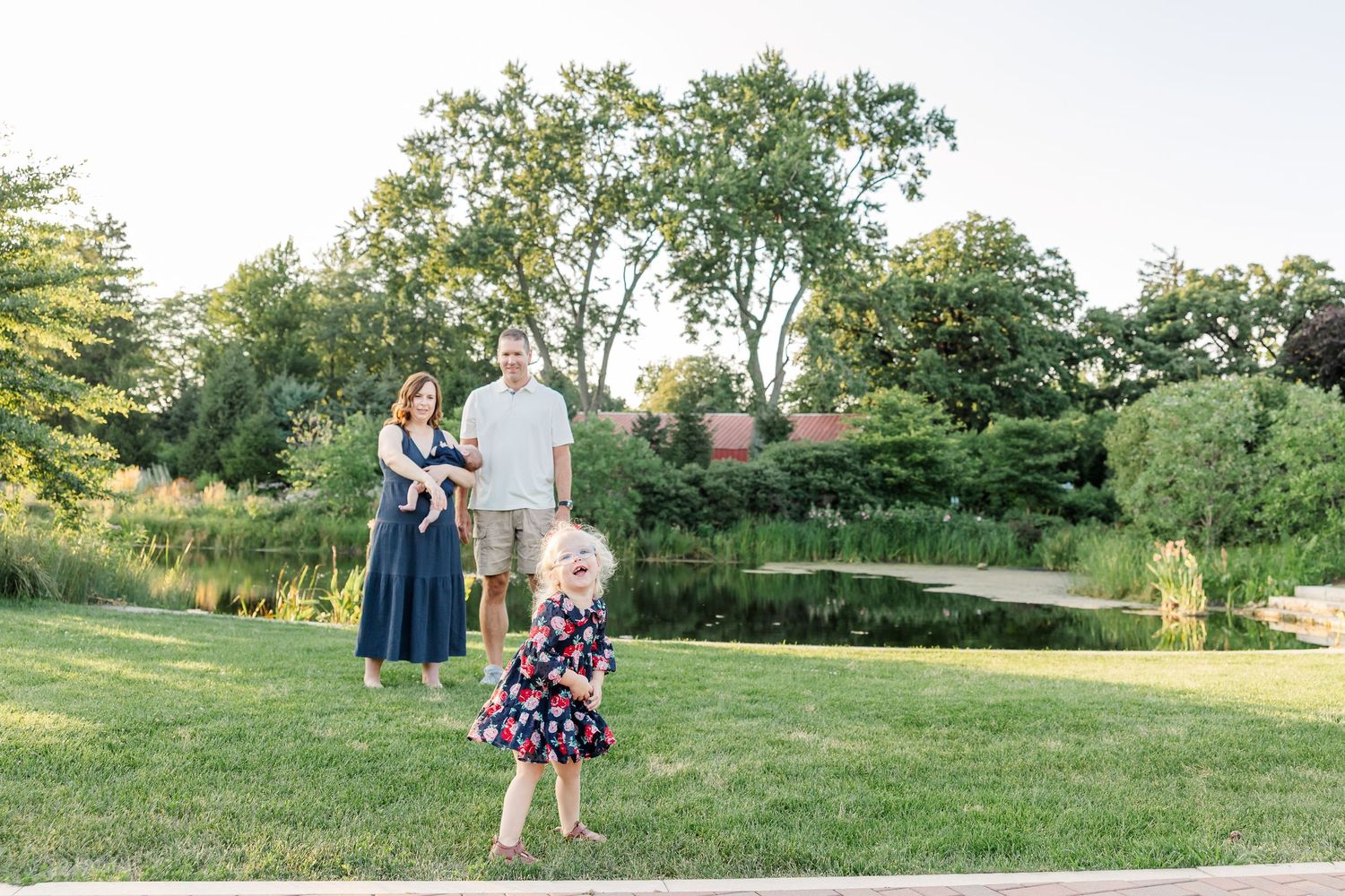 Caroline running toward the camera as Hilary and Andrew stand together near the Cantigny Park pond.