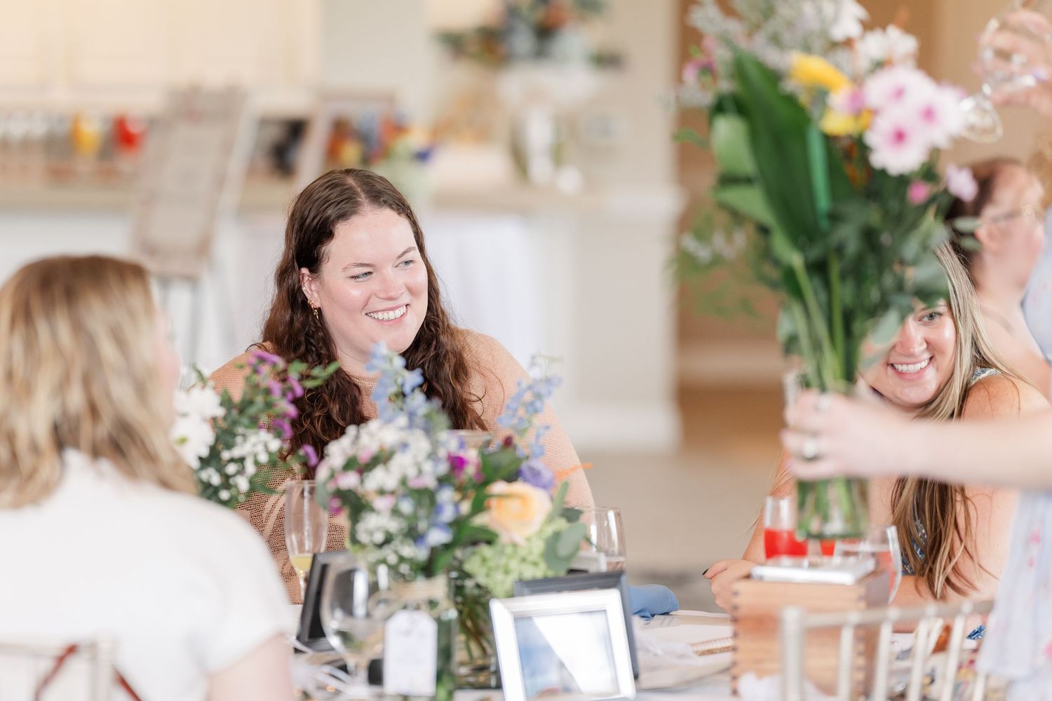 Happy women laughing together at a bridal shower table decorated with fresh floral arrangements.