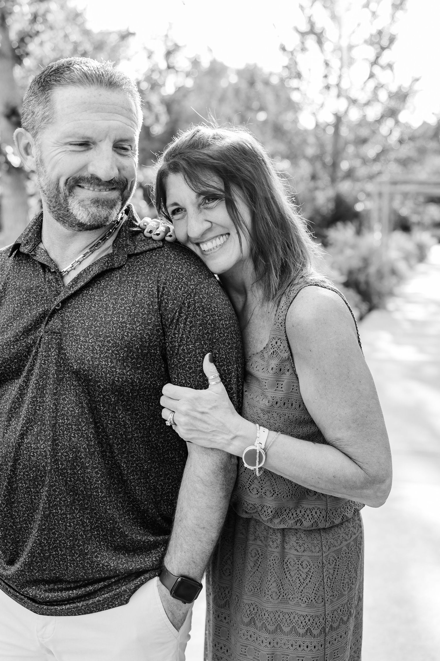Black and white photo of a smiling couple embracing outdoors, woman resting her head on mans shoulder.