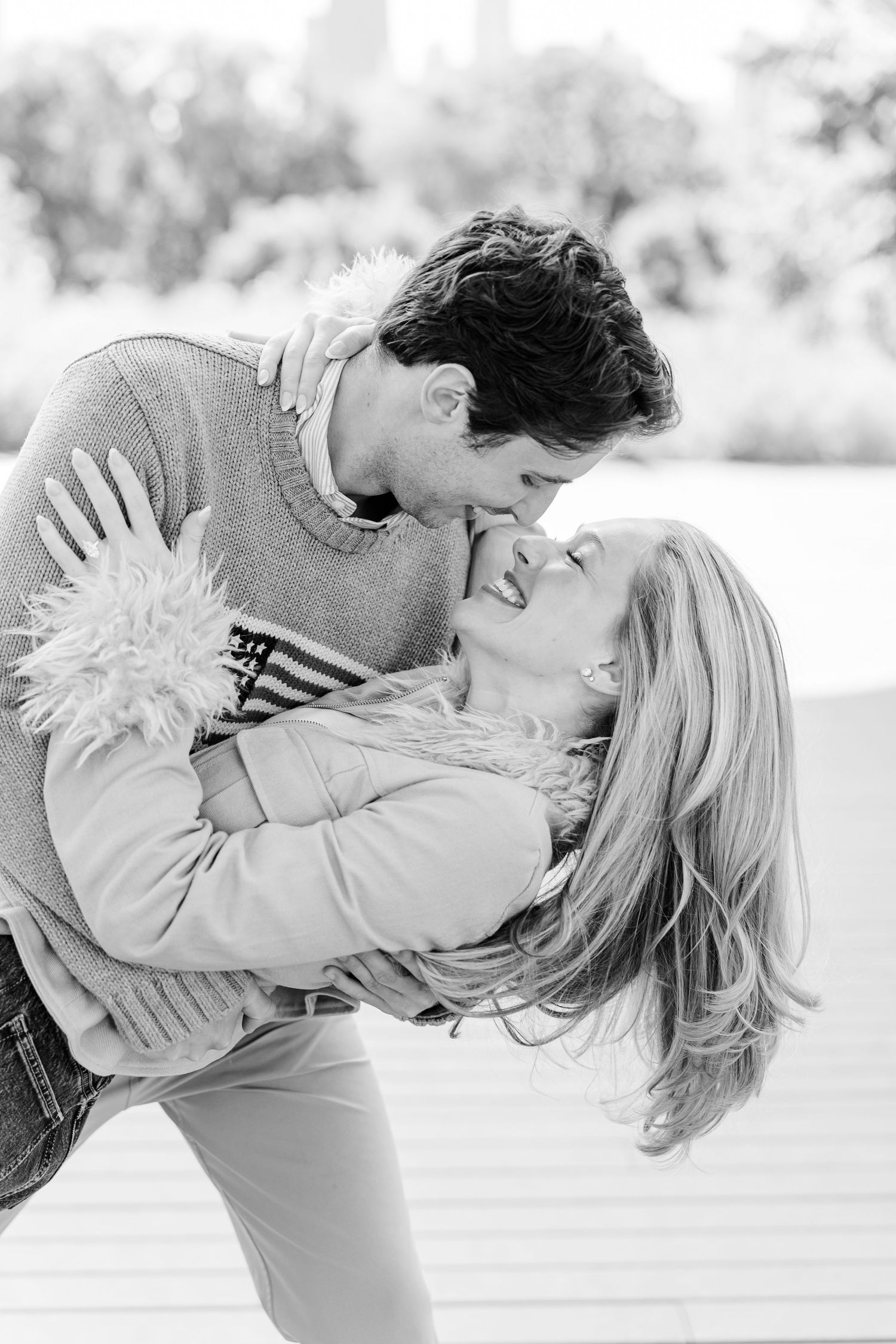 Black and white photo of a couple sharing a playful, romantic dip and kiss outdoors.